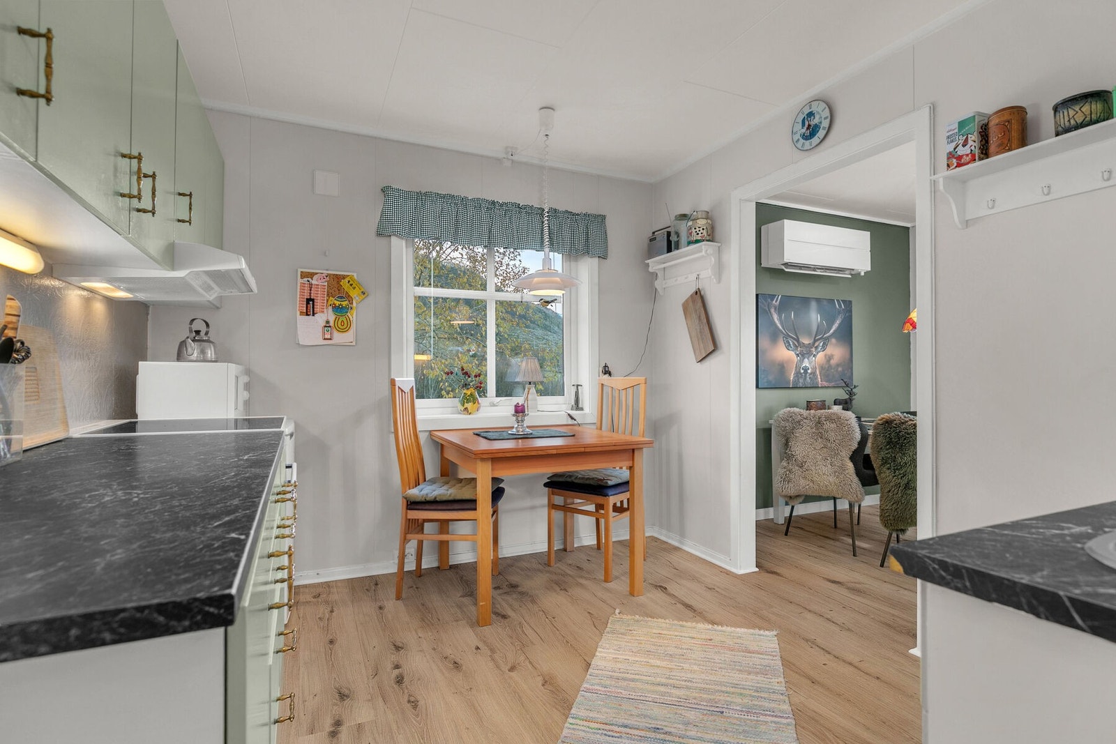 Kjøkkeninnredning med glatte og profilerte fronter i malt utførelse. Det er oppvaskmaskin og komfyr og et frittstående benkekjøleskap. Ventilator med avtrekk ut. Galleribilde