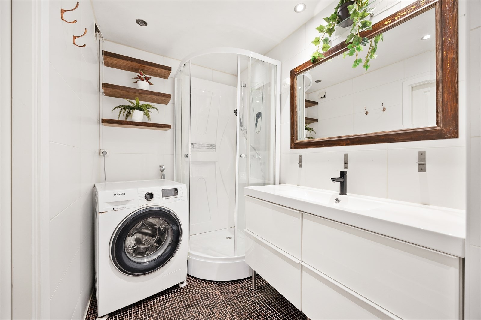 Badet inneholder dusjkabinett, opplegg for vaskemaskin, vegghengt klosett og stor servantseksjon med skuffer. Galleribilde