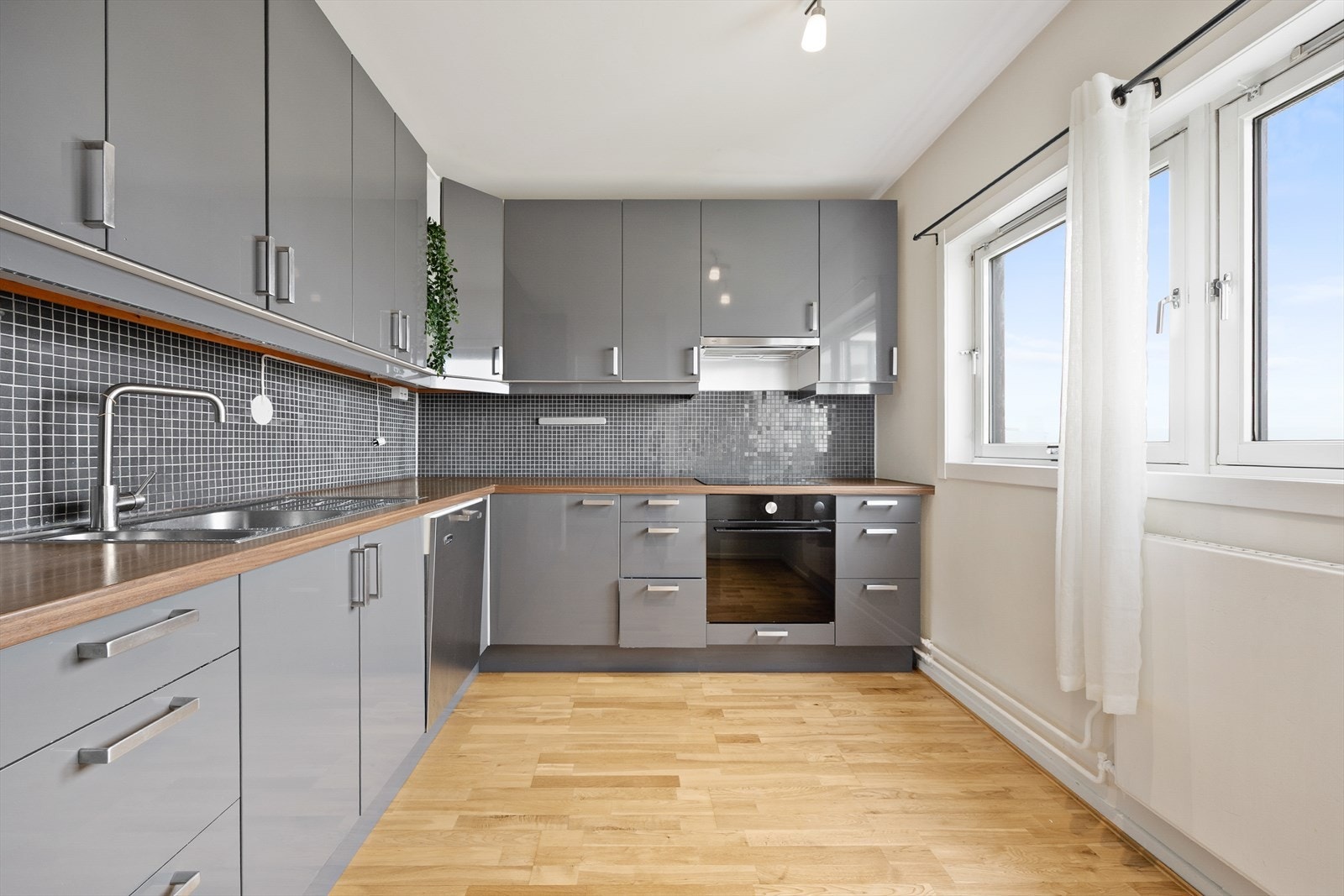 Kjøkkenet har integrert platetopp og stekeovn, frys-/kjøleskap og nedfelt oppvaskkum med fliser på vegg over benkeplate. Galleribilde