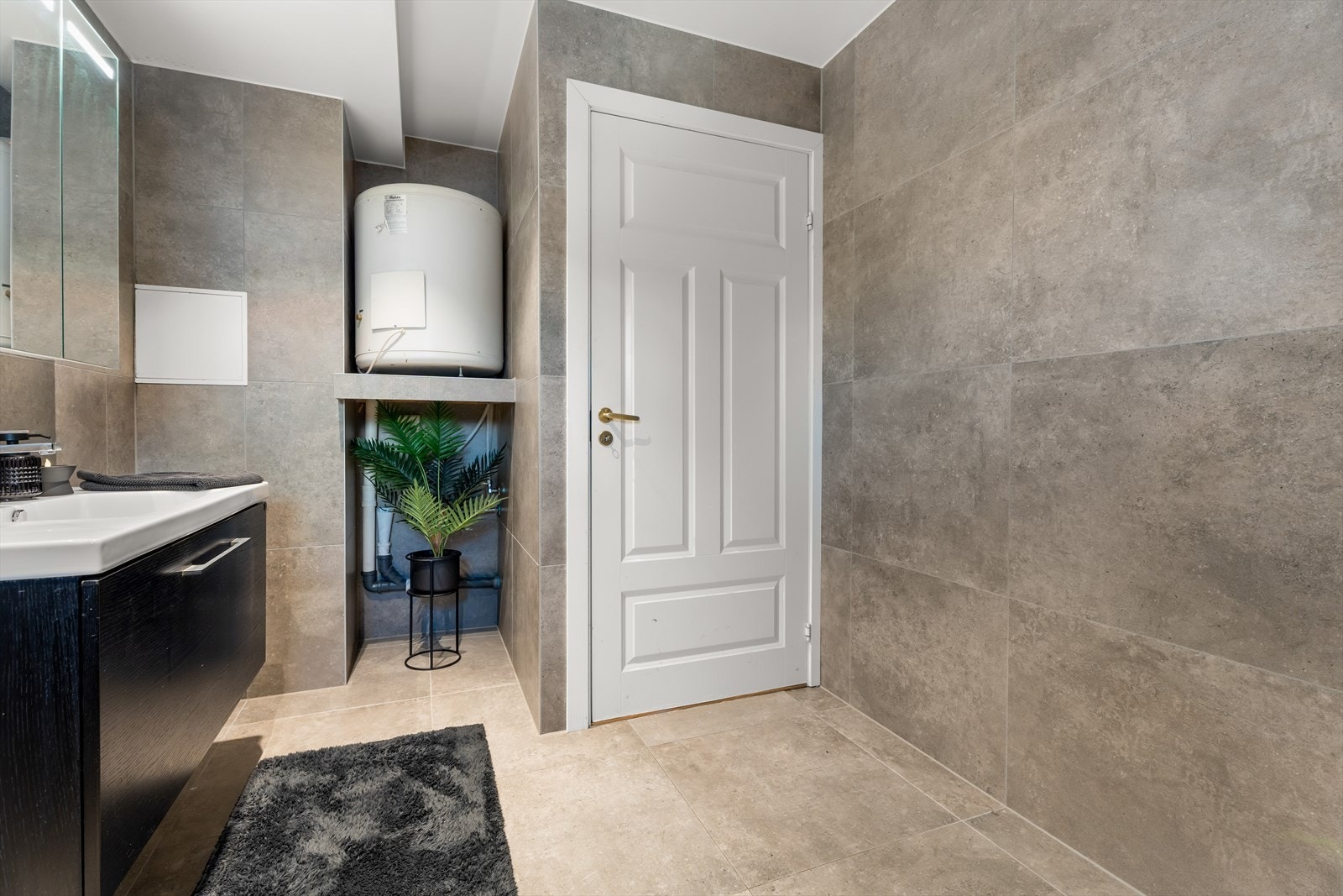 Badet er utstyrt med dusjhjørne, servant og speilskap med belysning, vegghengt toalett og opplegg til vaskemaskin. Galleribilde