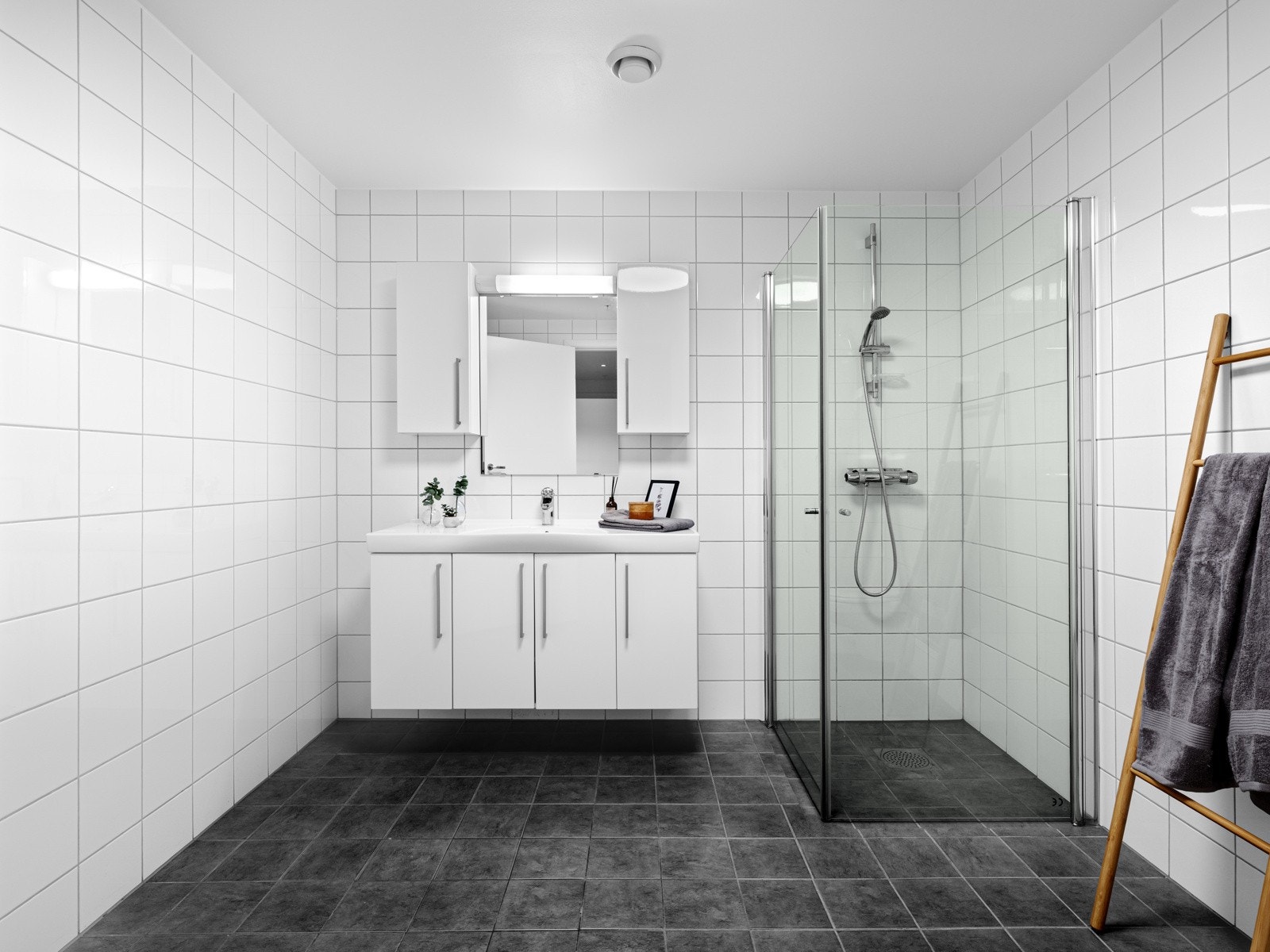 Vegghengt toalett, hvit baderomsinnredning med lagring, speil m/lys, innfellbare dusjdører i glass og opplegg til vaskemaskin Galleribilde