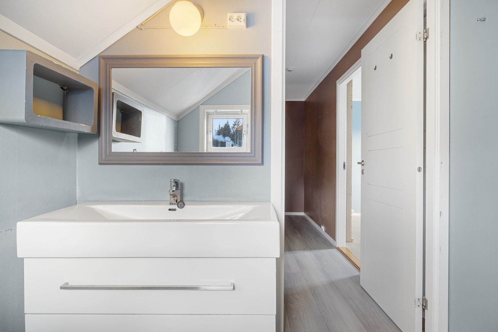 Moderne baderomsinnredning med skuffer og heldekkende servant, speil med belysning over. Baderommet er også utstyrt med dusjkabinett og gulvstående toalett. Galleribilde