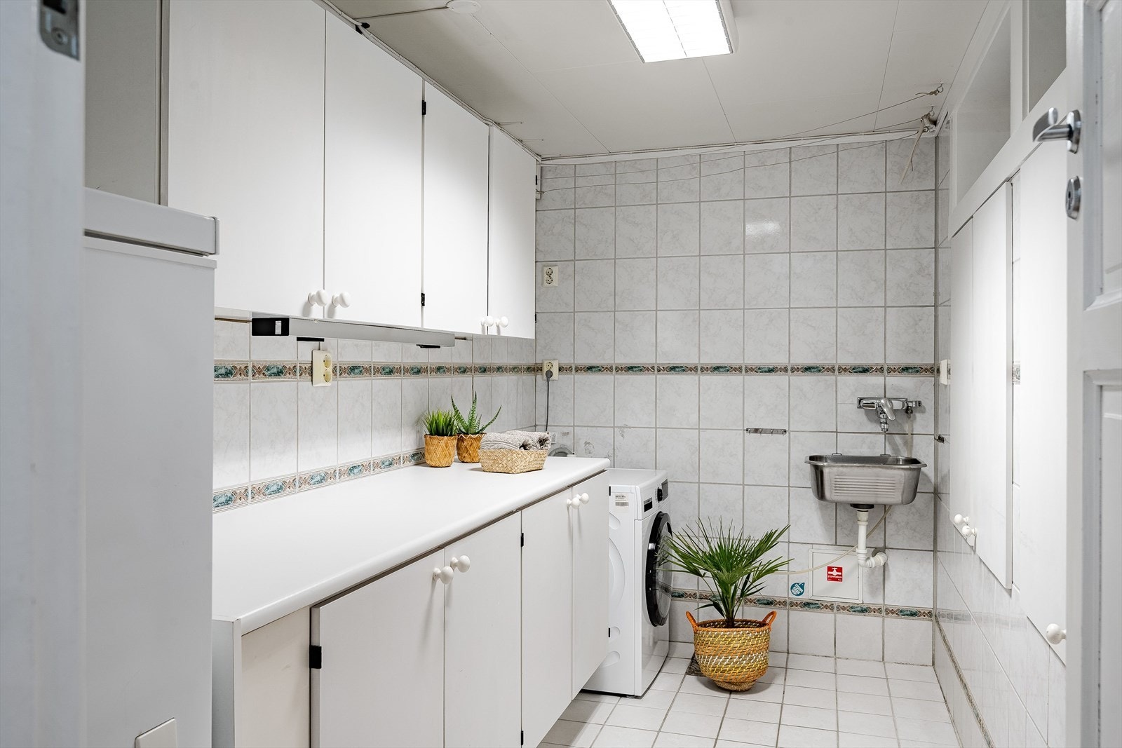 I kjelleren er det også et praktisk vaskerom med flislagte overflater. Rommet er utstyrt med lys innredning, vegghengt utslagsvask og opplegg for vaskemaskin. Galleribilde