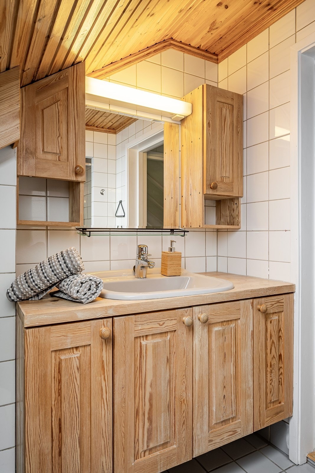 Heltre baderomsinnredning med profilerte fronter og nedfelt servant, speil med belysning og vegghengte skap over. Baderommet er også utstyrt med plassbygde skap i knevegg, dusjnisje med forheng og vegghengt toalett. Galleribilde