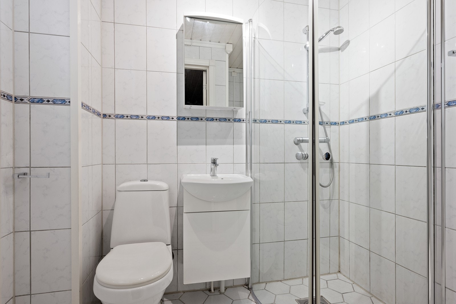 Badet er flislagt og innredet med dusjhjørne, toalett og servant. Galleribilde