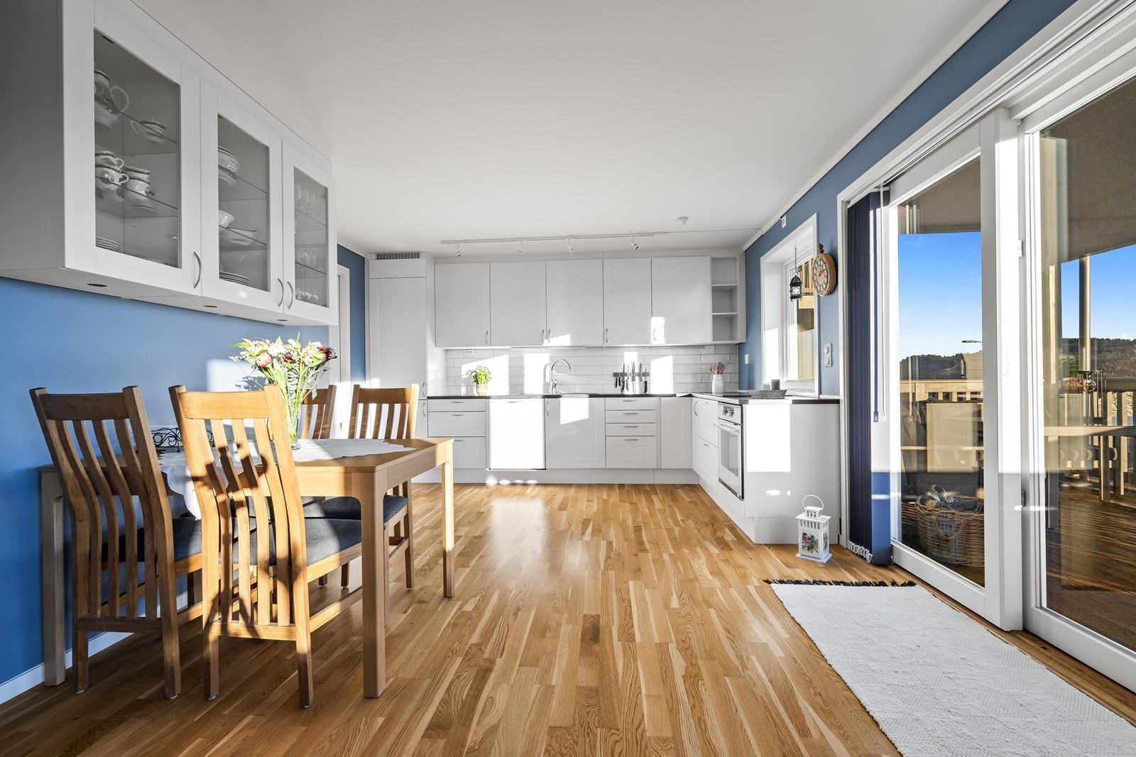 Kjøkkenet har en takhøy innredning med hvite, profilerte fronter, laminat benkeplate, integrerte hvitevarer og flis mellom overskap og benk. Galleribilde