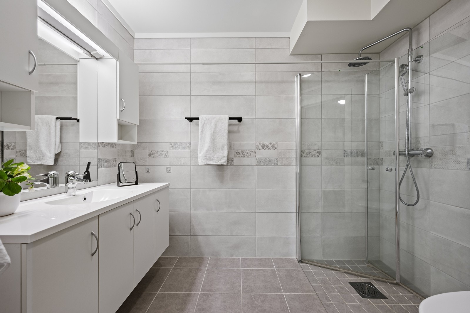 Stilrent og pent bad med vegghengt wc, dusjhjørne med glassdører og servant med over- og underskap. Galleribilde