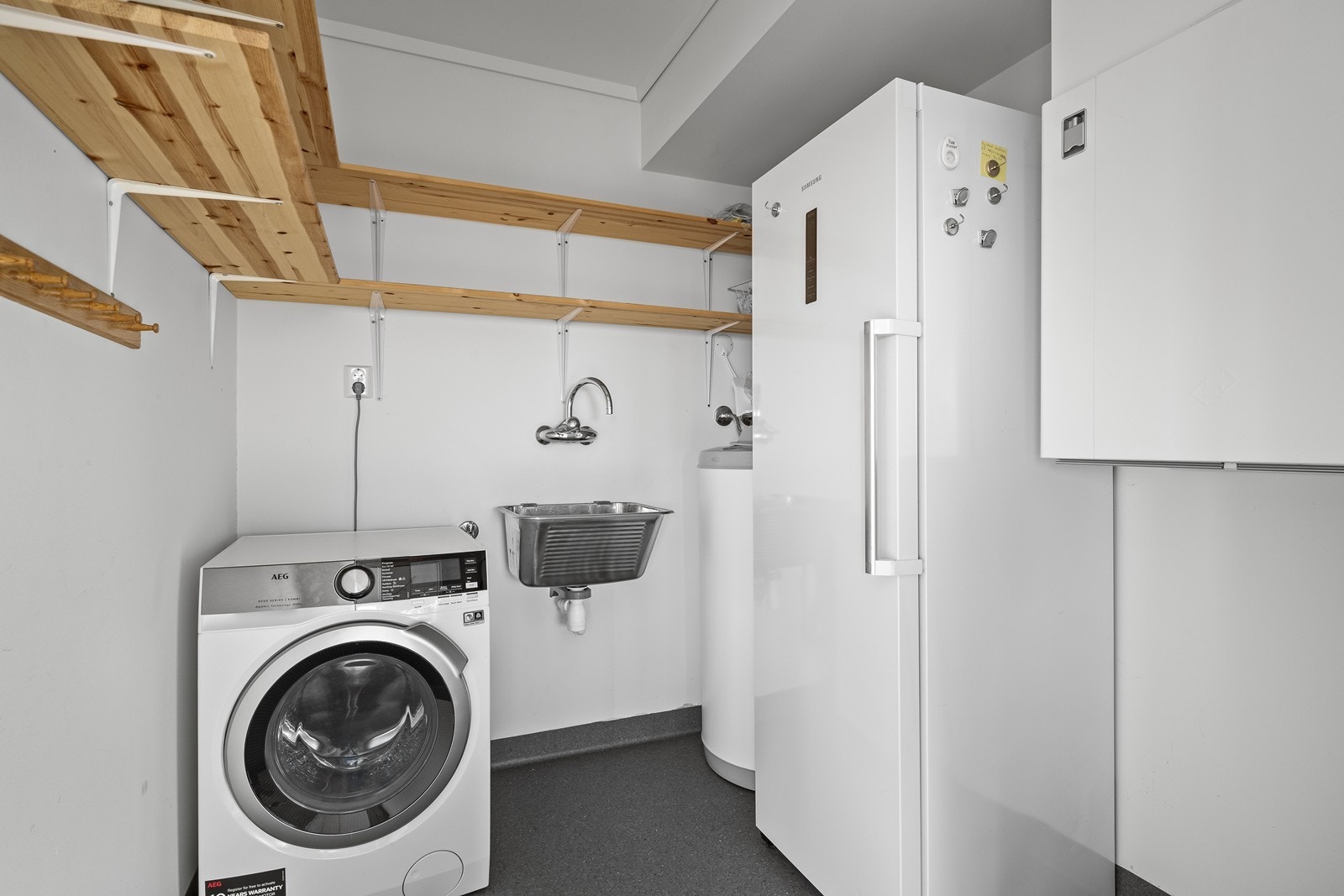 Praktisk bod/vaskerom med vegghyller, utslagsvask, varmtvannsbereder og opplegg for vaskemaskin. Galleribilde