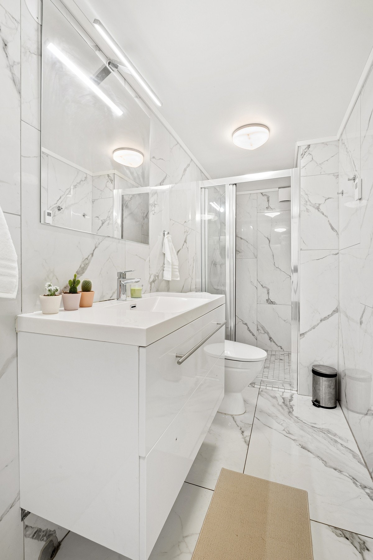 Innredningen består av servantinnredning, speil på vegg over servant, skap på vegg, toalett, skjermet dusjhjørne og opplegg for vaskemaskin. Galleribilde