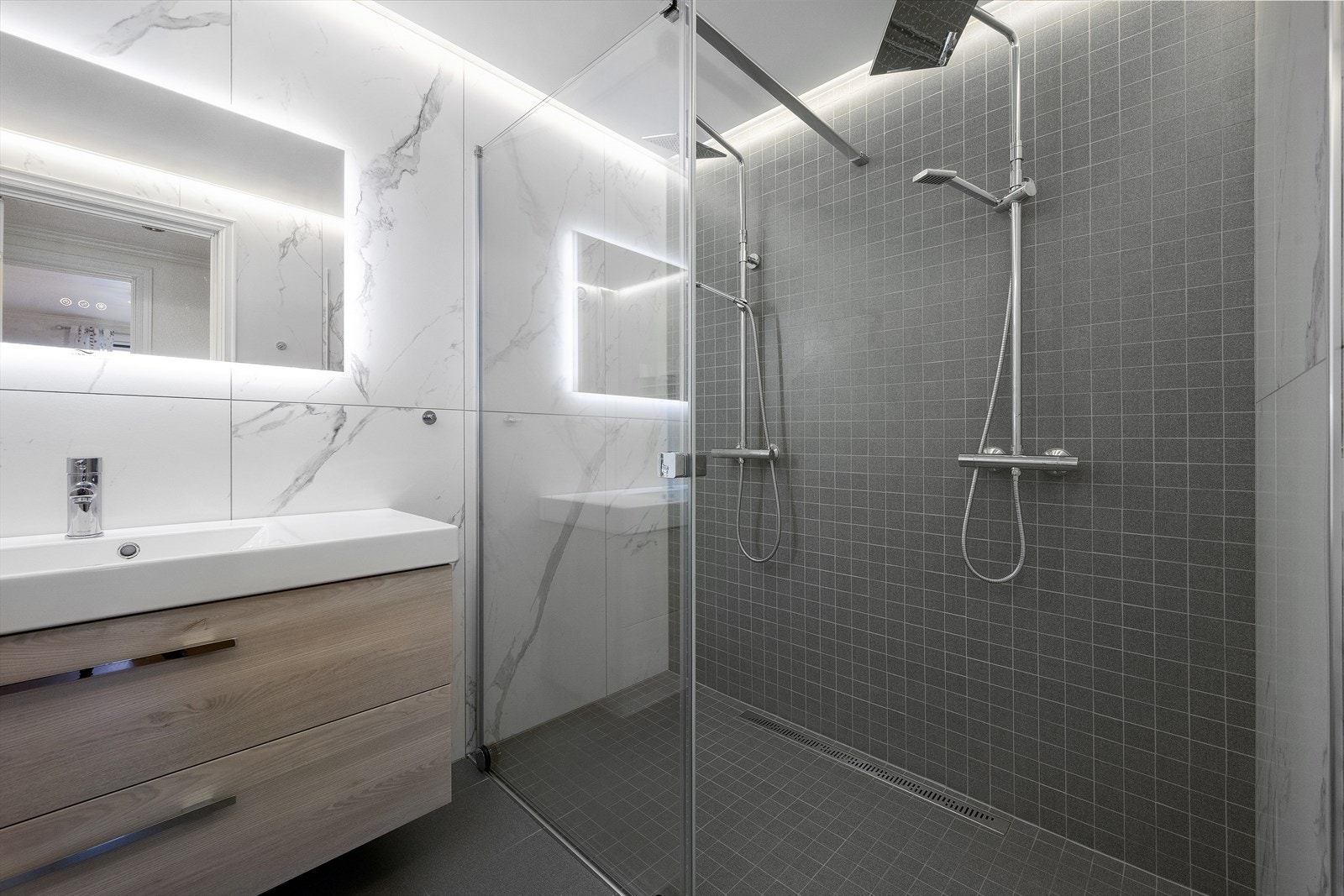 Badet er innredet dusjvegg med dobbel dusj, vegghengt toalett og innredning med servant. Galleribilde