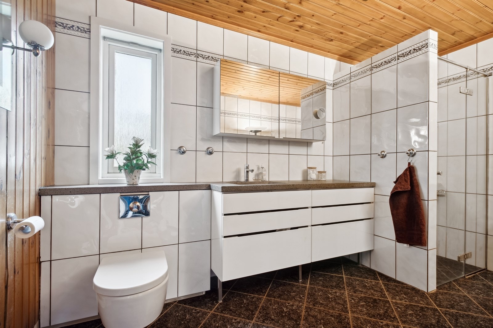 Ronslig flislagt bad med varmekabler i gulv. Vegghengt wc, servantinnredning med speilskap og dusjnisje. Galleribilde