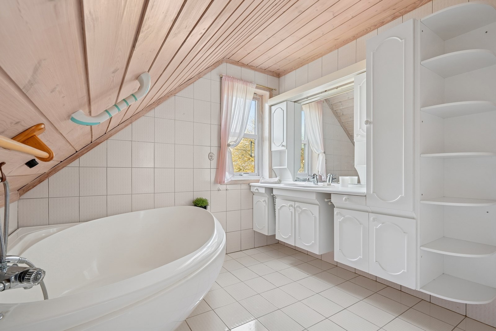 Baderommet er helfliset med lyse fliser på gulv og vegger. I gulvet har man også varmekabler for ekstra komfort. Badet er ellers utstyrt med badekar, toalett og stor veggseksjon med nedfelt servant. Galleribilde