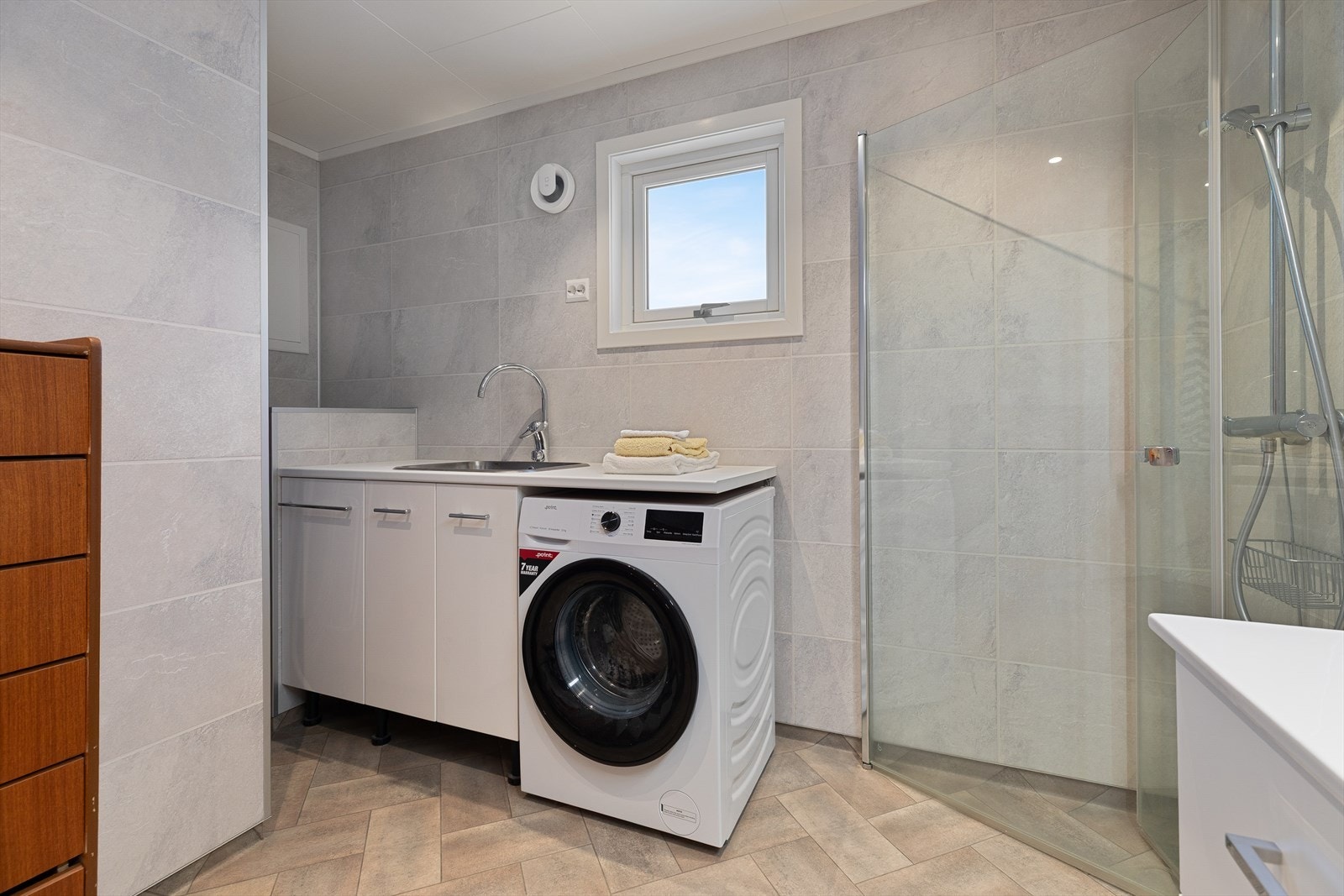 Badet har dusjhjørne, veggmontert toalett, servantinnredning, utslagsvask og innebygd varmtvannstank. Galleribilde