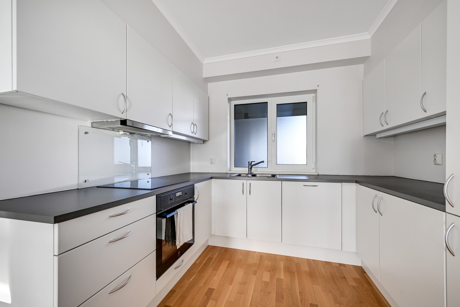 Kjøkkenet har en fin innredning med hvite, slette fronter. Benkeplaten er i laminat, og det er montert glass over platetoppen. Galleribilde