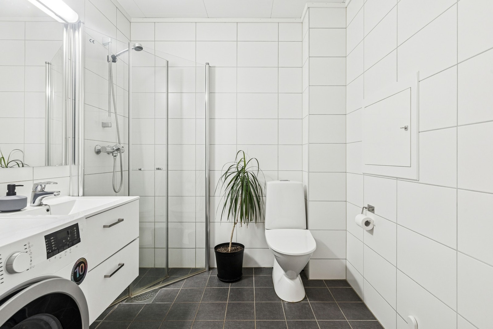 Baderom fra byggeår. Flislagt gulv med gulvvarme. Flislagte vegger. Malt himlingsflate. Vegghengt servantskap med heldekkende servant og ettgreps armatur. Galleribilde