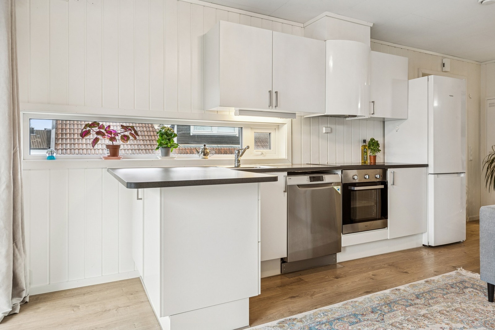 Kjøkken med åpen løsning mot stue. Kjøkkeninnredning med hvite slette fronter fra byggeår. Benkeplater av laminat. Galleribilde