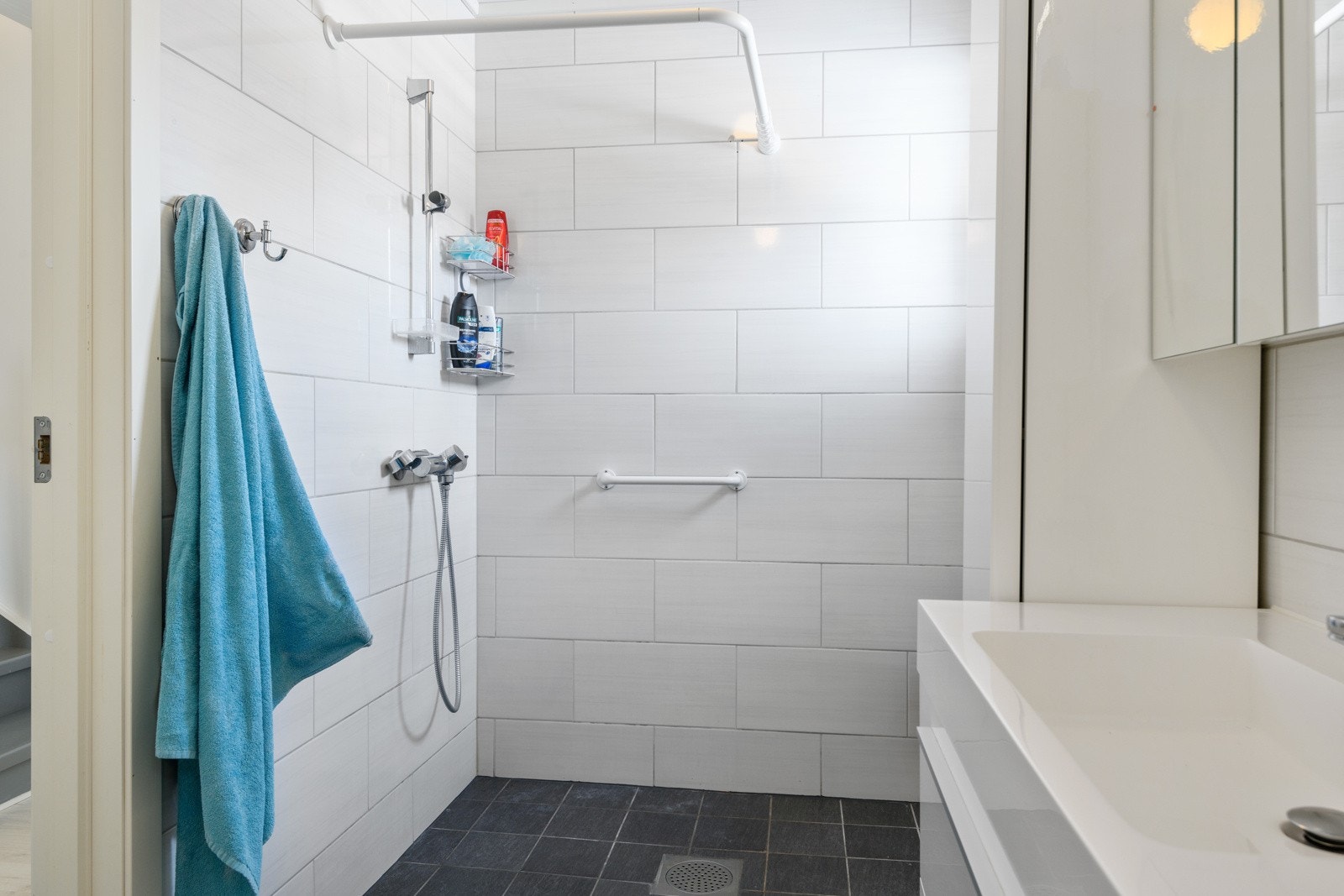 Moderne baderomsinnredning med skuffer og heldekkende servant, speil med integrert belysning over. Baderommet er også utstyrt med dusjhjørne med forheng og gulvmontert toalett. Plass og opplegg for vaskemaskin og tørketrommel over om ønskelig. Galleribilde