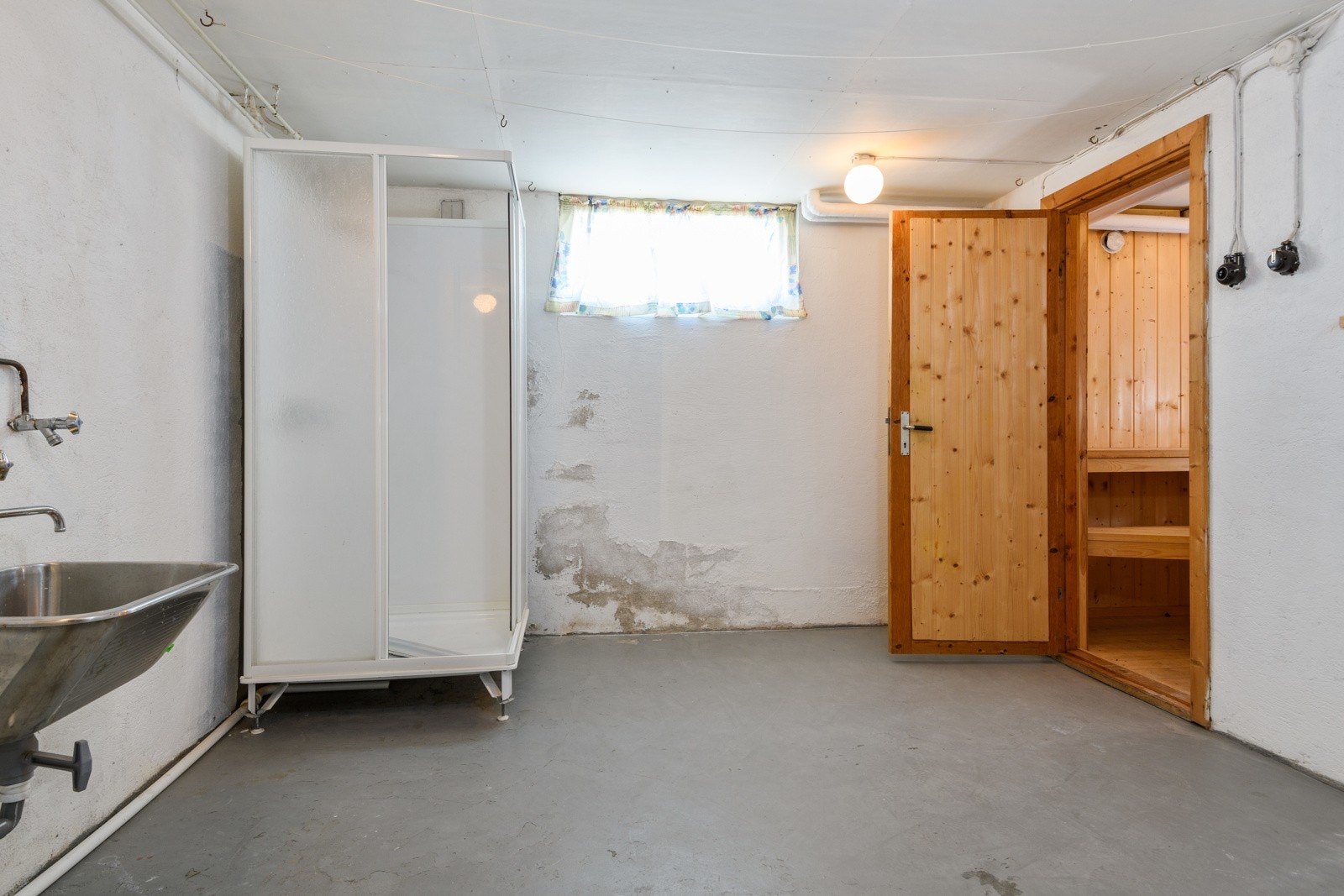 Bad/vaskerom i kjeller med støpt gulv og overflater med malt murpuss, antatt fra byggeåret. Rommet er utstyrt med dusjkabinett, utslagskum og sluk. Galleribilde