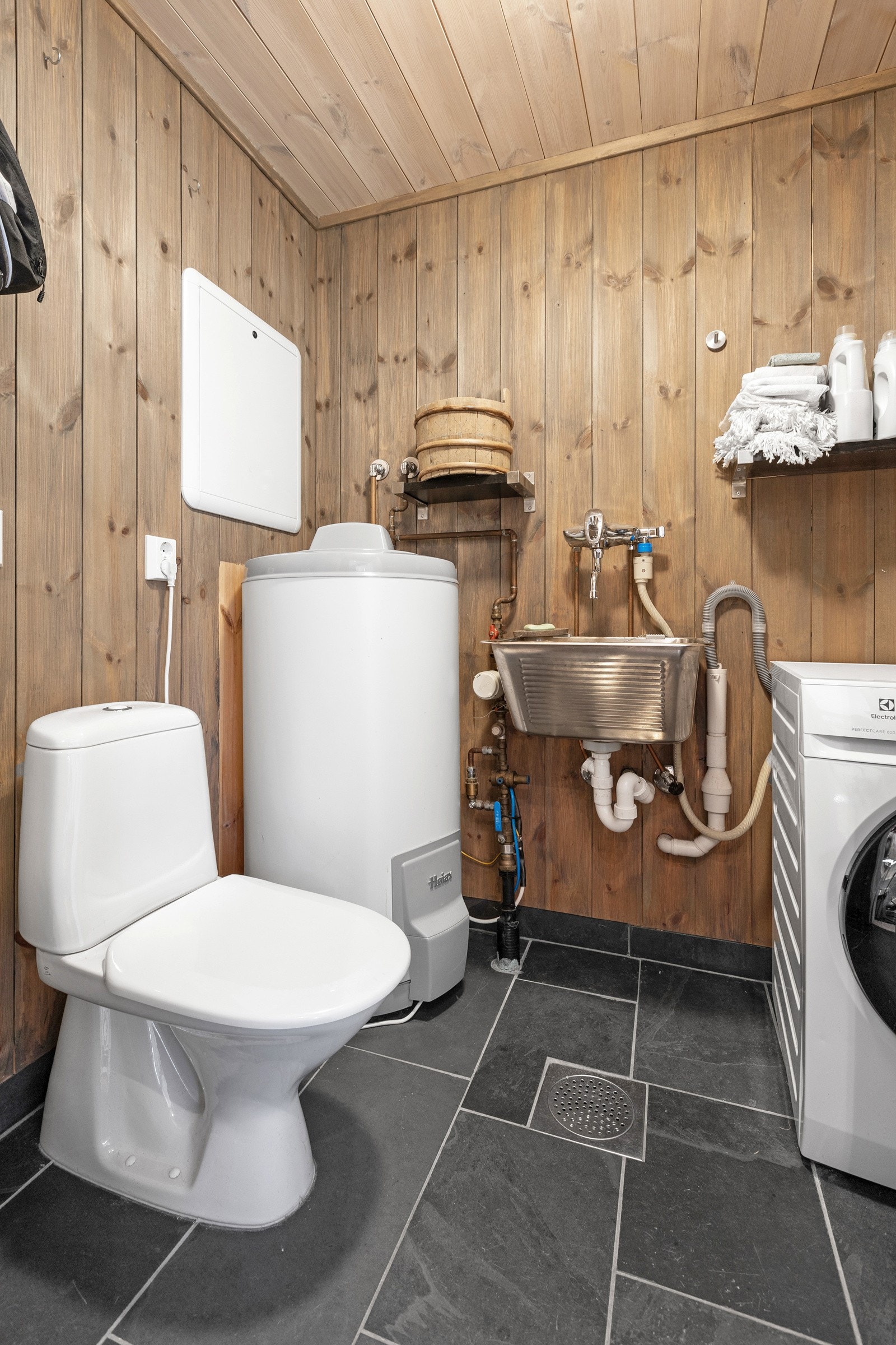 Separat toalettrom/vaskerom med flislagt gulv som har opplegg for vaskemaskin. Varmtvannsbereder er plassert her. Galleribilde