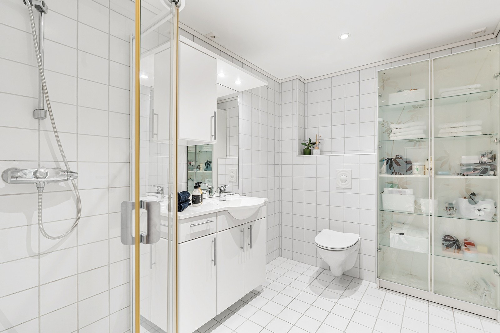 Badet er av god størrelse og er innredet med dusjvegger i glass, vask med skapinnredning og speil, samt vegghengt toalett. Galleribilde