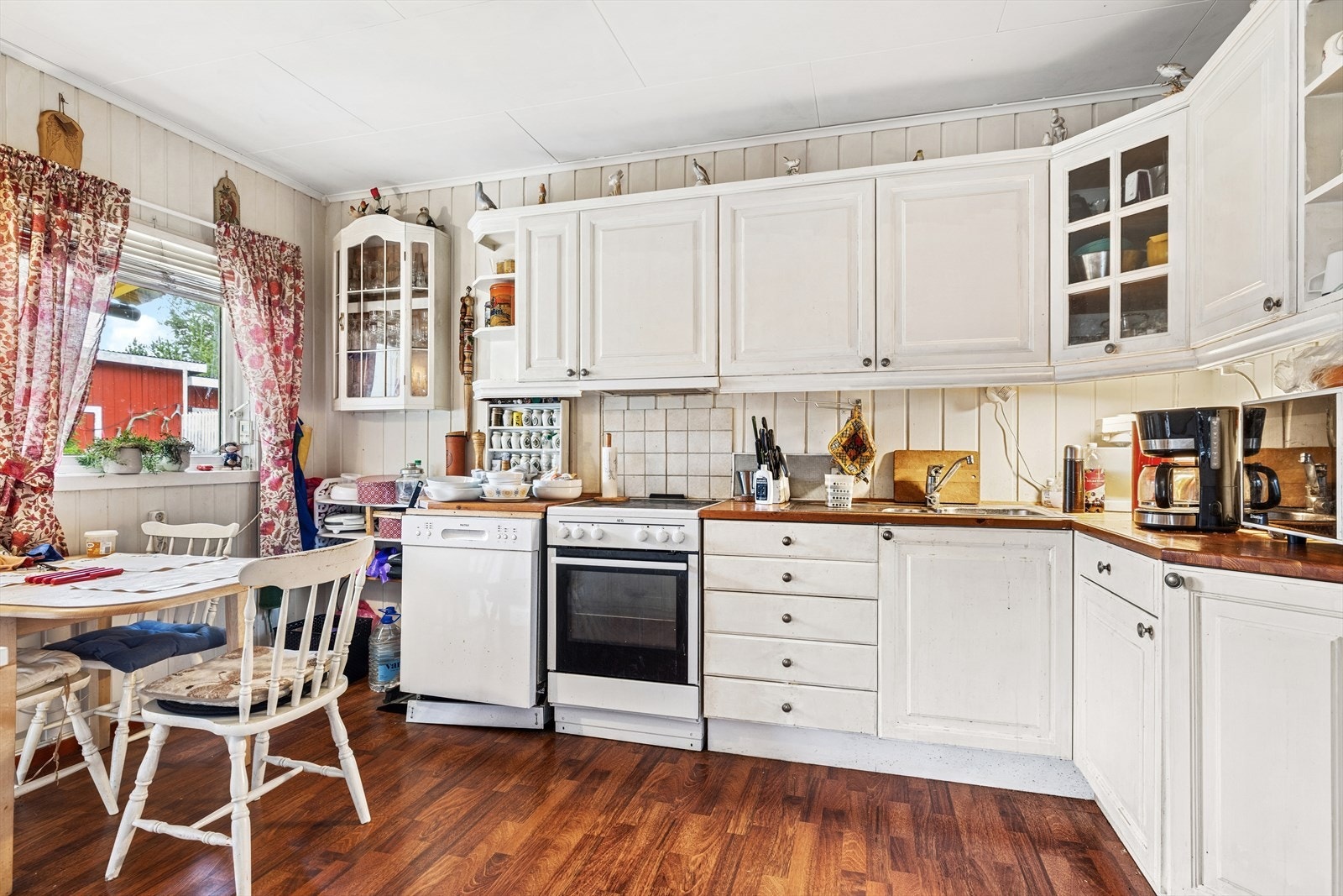 Kjøkkeninnredning av furu fra eldre dato, malt i ettertid. Plass for frittstående oppvaskmaskin, kjøleskap og komfyr. Mekanisk avtrekk over kokesone med avtrekk ut i yttervegg. Galleribilde