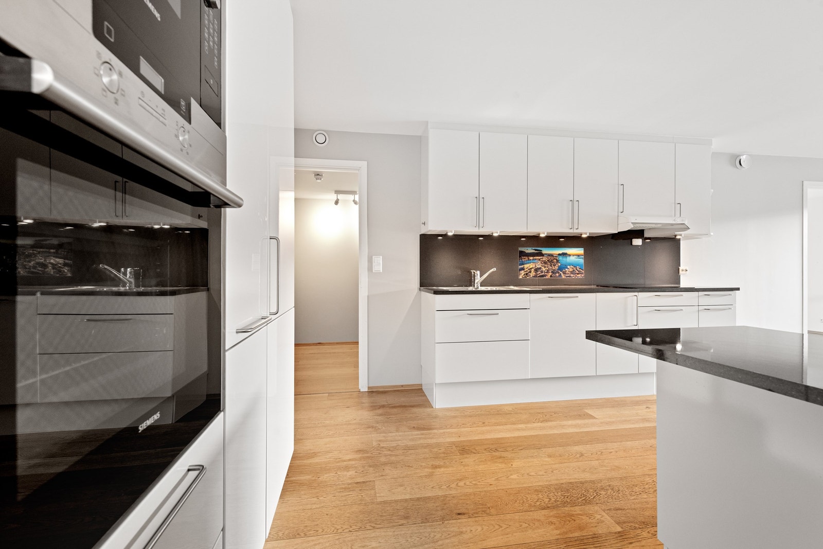 Kjøkkenet har induksjon koketopp, integrert kjøleskap, stekeovn (SIEMENS), micro (SIEMENS) i høyskap, oppvaskmaskin og hvitlakkert ventilator. Fliser over kjøkkenbenk. Det er ettermontert kjøkkenøy i 2021 med vitrineskap. Galleribilde