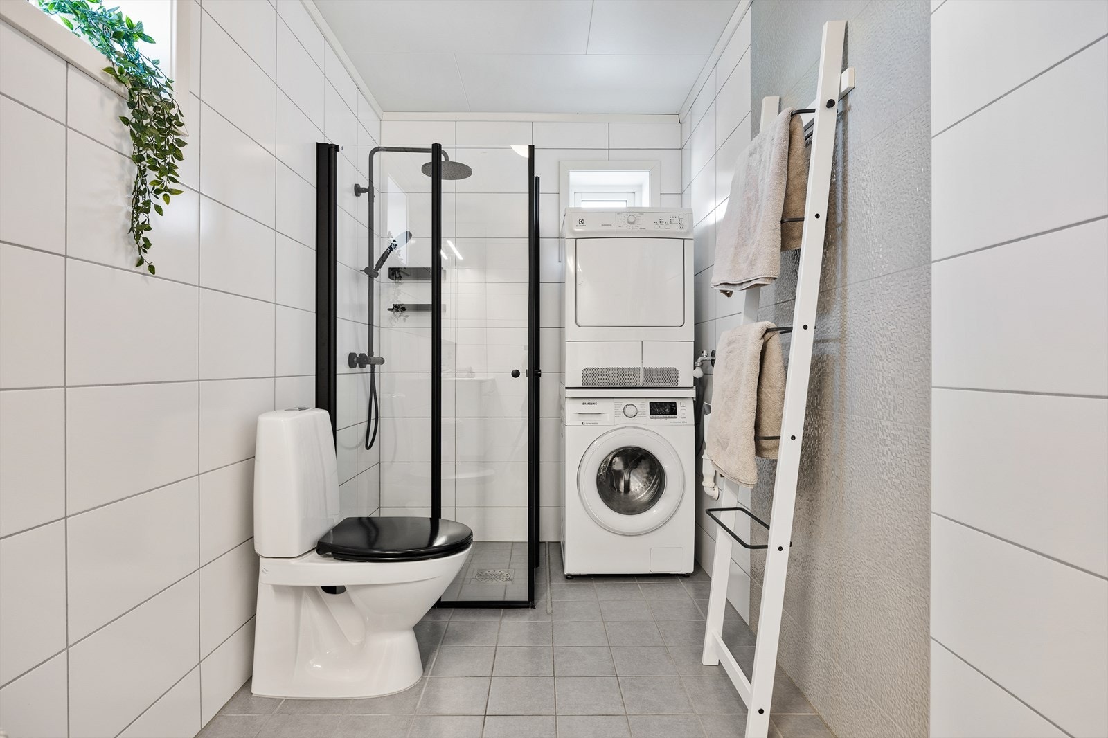 Rommet er innredet med servanskap med glatte fronter og hvit vask, speil, toalett, dusjhjørne med innfellbare dører og opplegg for vaskemaskin/tørketrommel. Galleribilde