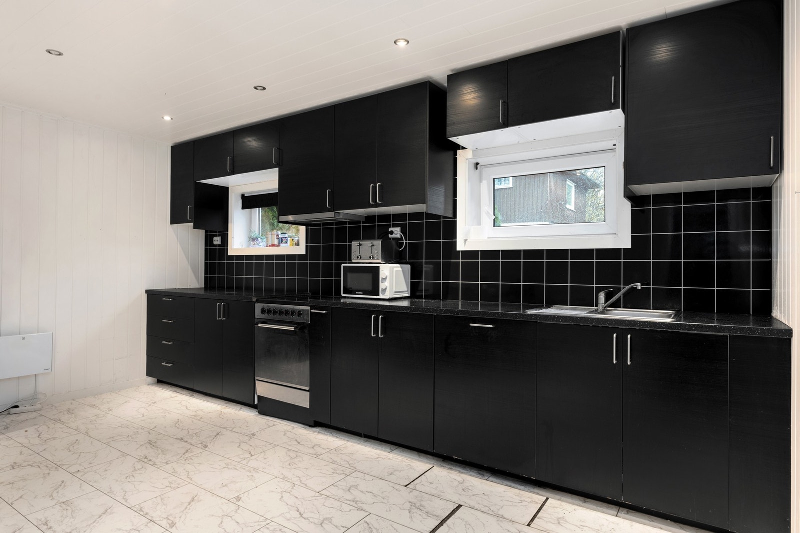 Kjøkkeninnredning med finerte fronter, laminat benkeplater, oppvaskkum, ventilator, plater over benk, belysning under overskap og opplegg for oppvaskmaskin. Galleribilde