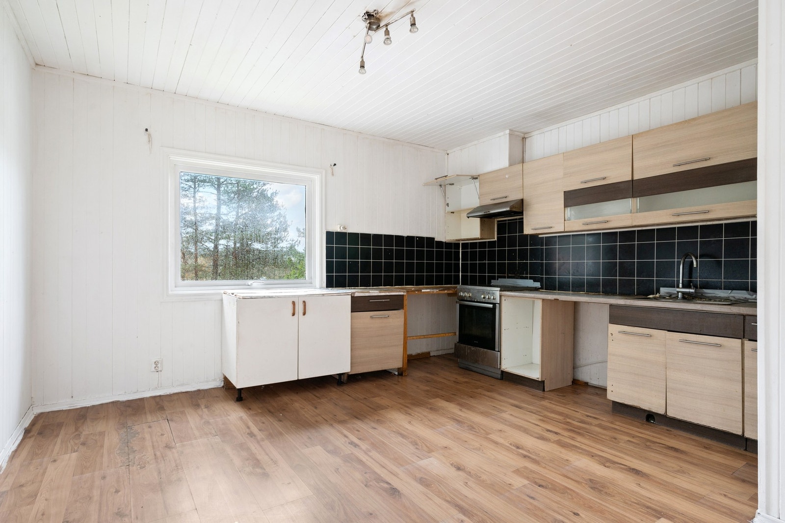 Kjøkkeninnredning med finerte fronter, laminat benkeplater, oppvaskkum, ventilator, plater over benk og opplegg for oppvaskmaskin. Galleribilde