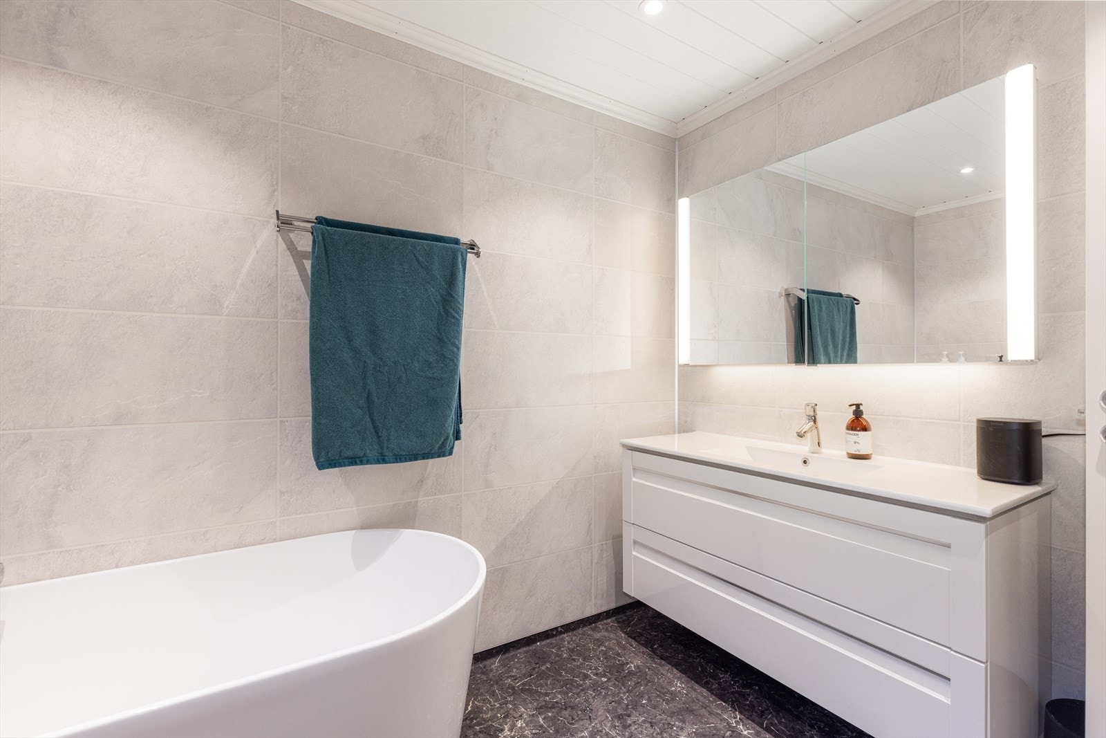 Hvit innredning med dype skuffer og heldekkende servant, samt speil med integrert lys som gir et stilrent uttrykk kombinert med varm og behagelig belysning. Rehabiliteringen er utført av firma og bygget opp fra grunnen, med nytt gulv, vegger og tak. Galleribilde