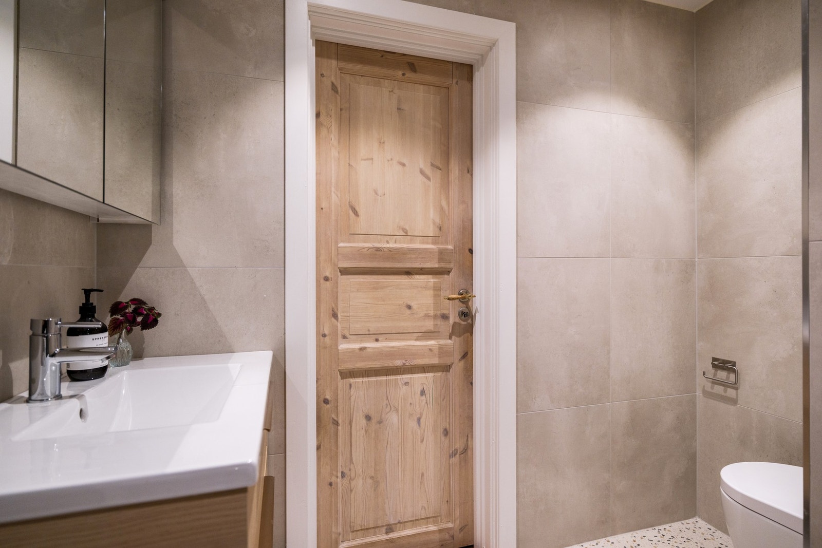 Inneholder: Heldekkende servant med skuffer, speilskap, dusjhjørne med regnfallsdusj og leddede glassdører, vegghyller, vegghengt klosett, og opplegg til vaskemaskin. Galleribilde