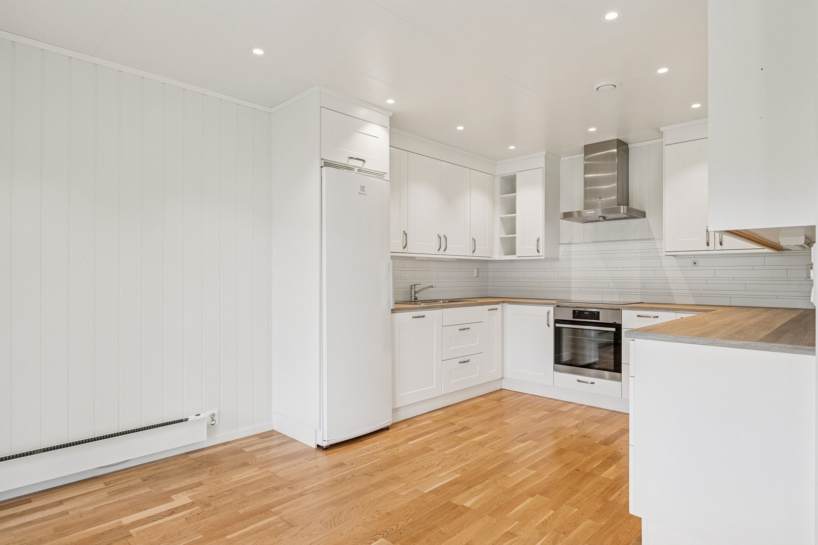 Kjøkkenet fremstår som lyst, innbydende og svært funksjonelt. Det klassiske hvite kjøkkenet med rene linjer og profilerte fronter gir et tidløst uttrykk, Benkeplatene i treverk gir en varm kontrast til det hvite og skaper en naturlig balanse i rommet. Galleribilde