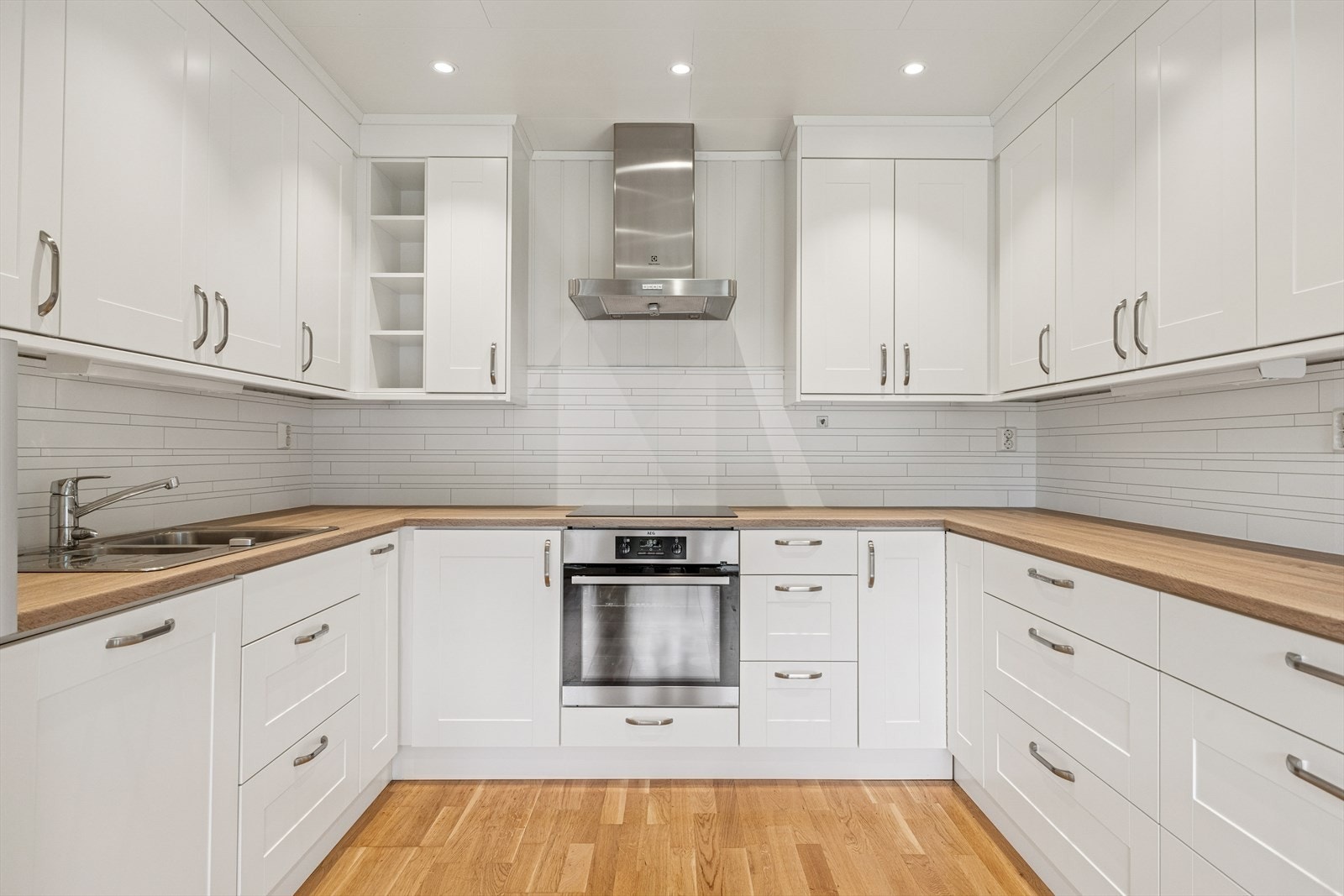 Kjøkkenet er utformet i en praktisk U-løsning, som gir rikelig med både benkeplass og oppbevaringsmuligheter. Over- og underskap gir god lagringsplass for alt av kjøkkenutstyr, og åpne hyller gir mulighet for dekor eller enkel tilgang til mindre ting. Galleribilde