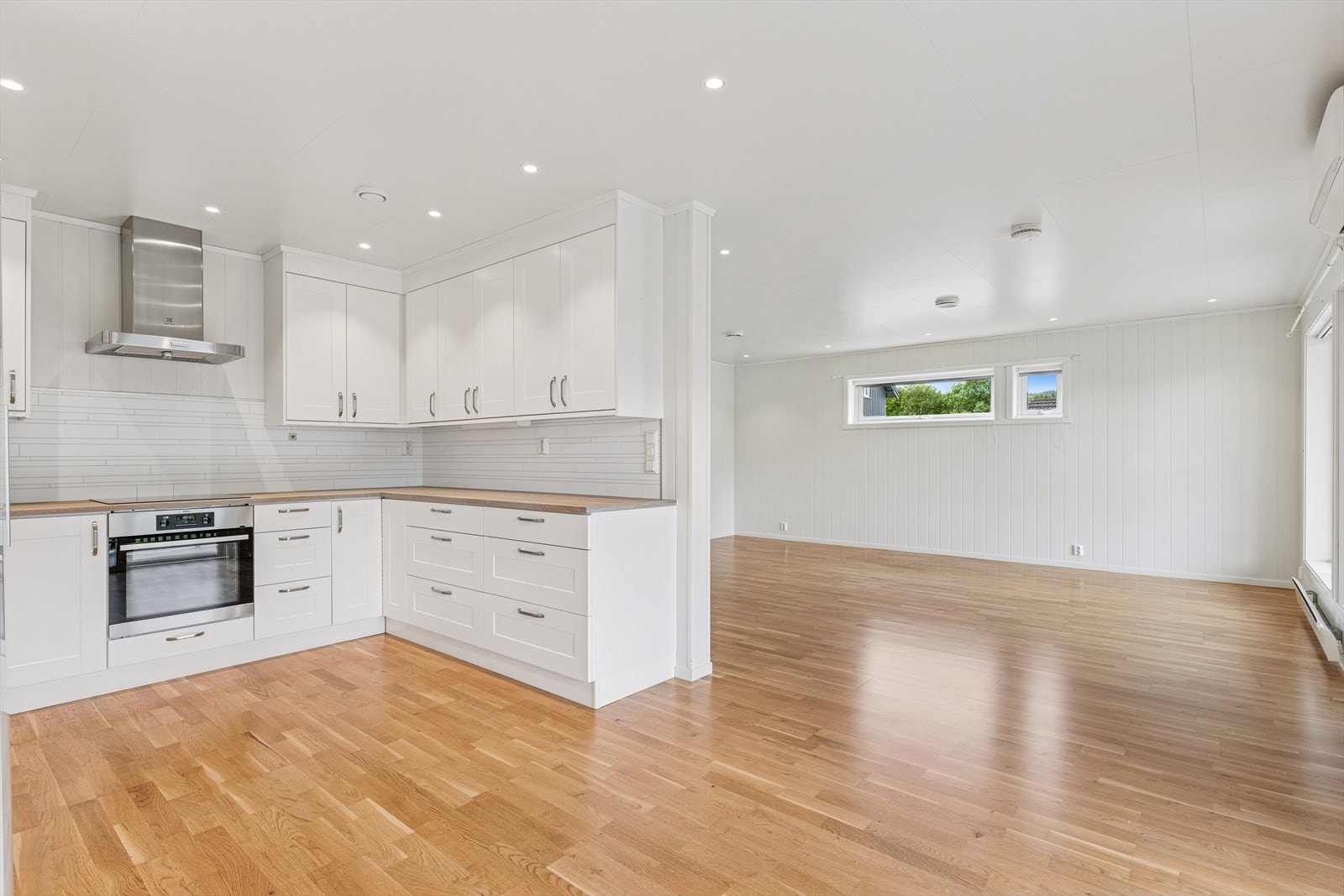 Overgangen fra kjøkken til stue er sømløs, og parkettgulvet strekker seg gjennom hele rommet og binder sonene sammen på en harmonisk måte. Stueområdet er lyst og romslig, med store vindusflater og god takhøyde som slipper inn rikelig med dagslys. Galleribilde