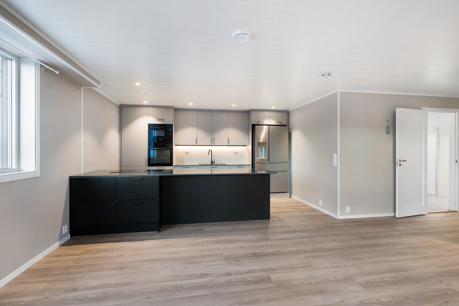 Det moderne kjøkkenet har en stor kjøkkenøy med induksjonstopp og integrert ventilator med kullfilter, noe som gir et stilrent uttrykk uten behov for takmontert avtrekk. Galleribilde