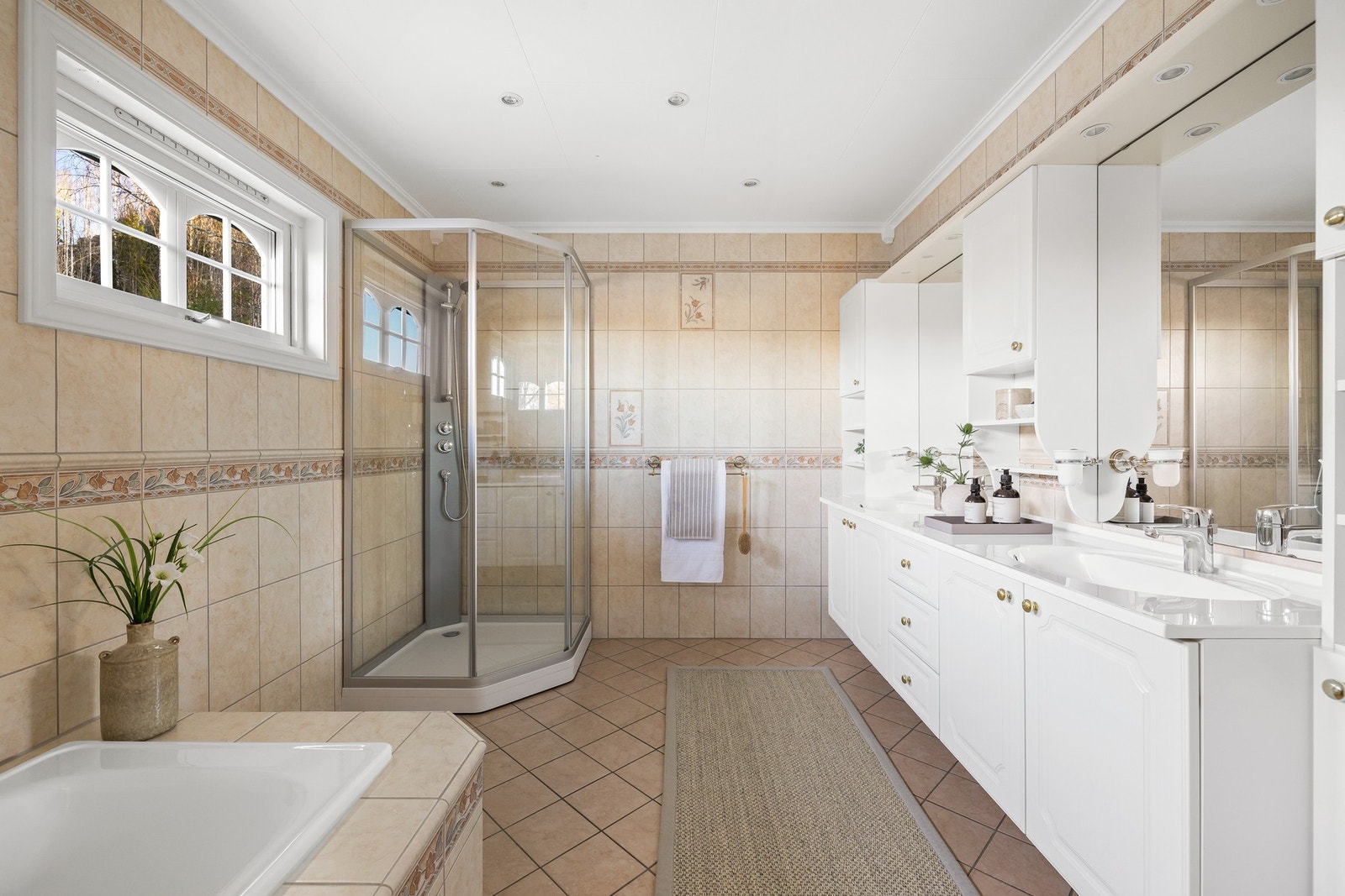 Boligen har et stort flislagt baderom innredet dusj, badekar og dobbel servant Galleribilde