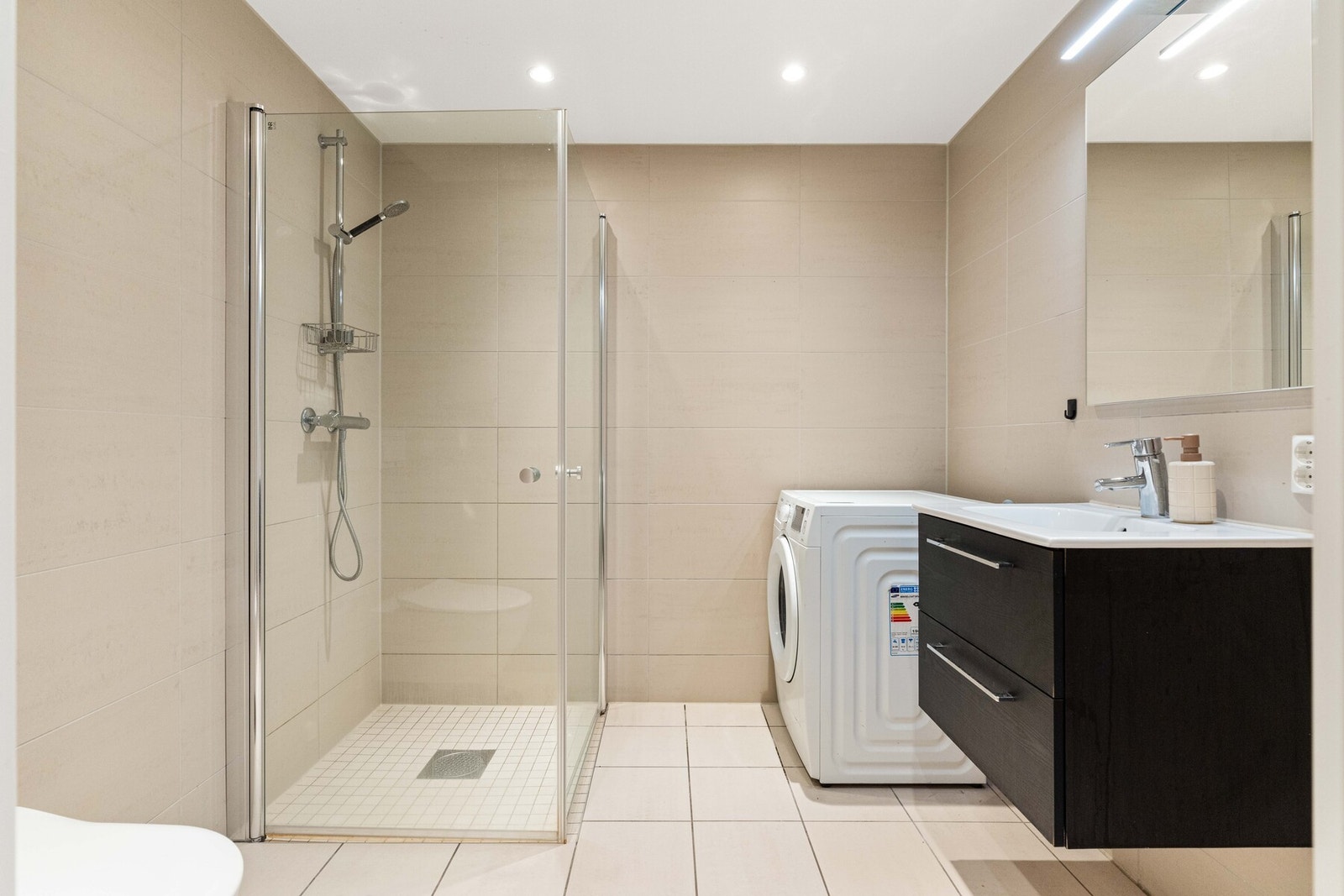 Fra entreen finner vi badet. Badet er svært delikat og er innredet med benkeskap, dusj med dører i herdet glass, veggfestet klosett og opplegg for vaskemaskin. Varme i gulv og downlights i himling. Galleribilde