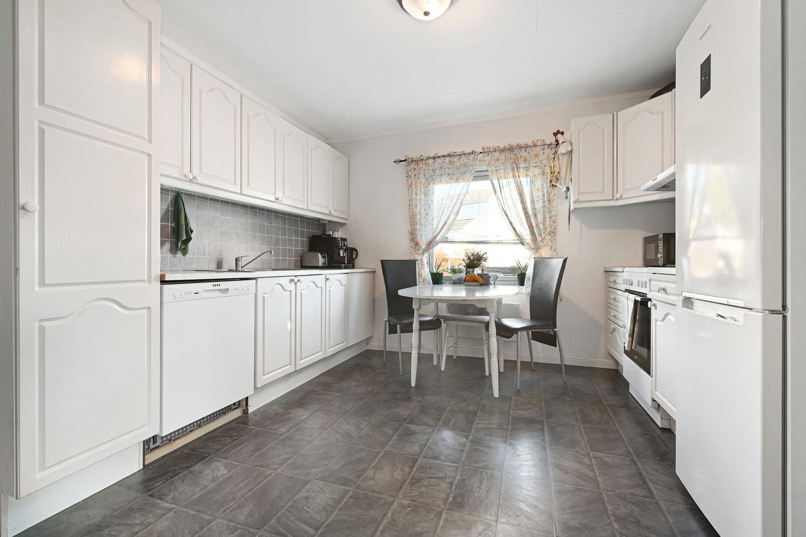 Kjøkkenet har profilerte fronter og laminat benkeplate. Frittstående komfyr og kjøl/fryseskap, underbygget oppvaskmaskin. Galleribilde