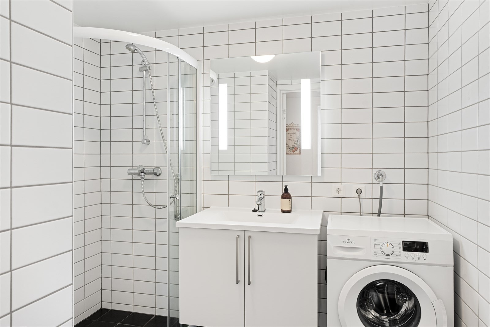Pent, helfliset bad/vaskerom som er innredet med servant nedfelt i møbel, gulvmontert toalett, dusjløsning med dører og opplegg for vaskemaskin Galleribilde