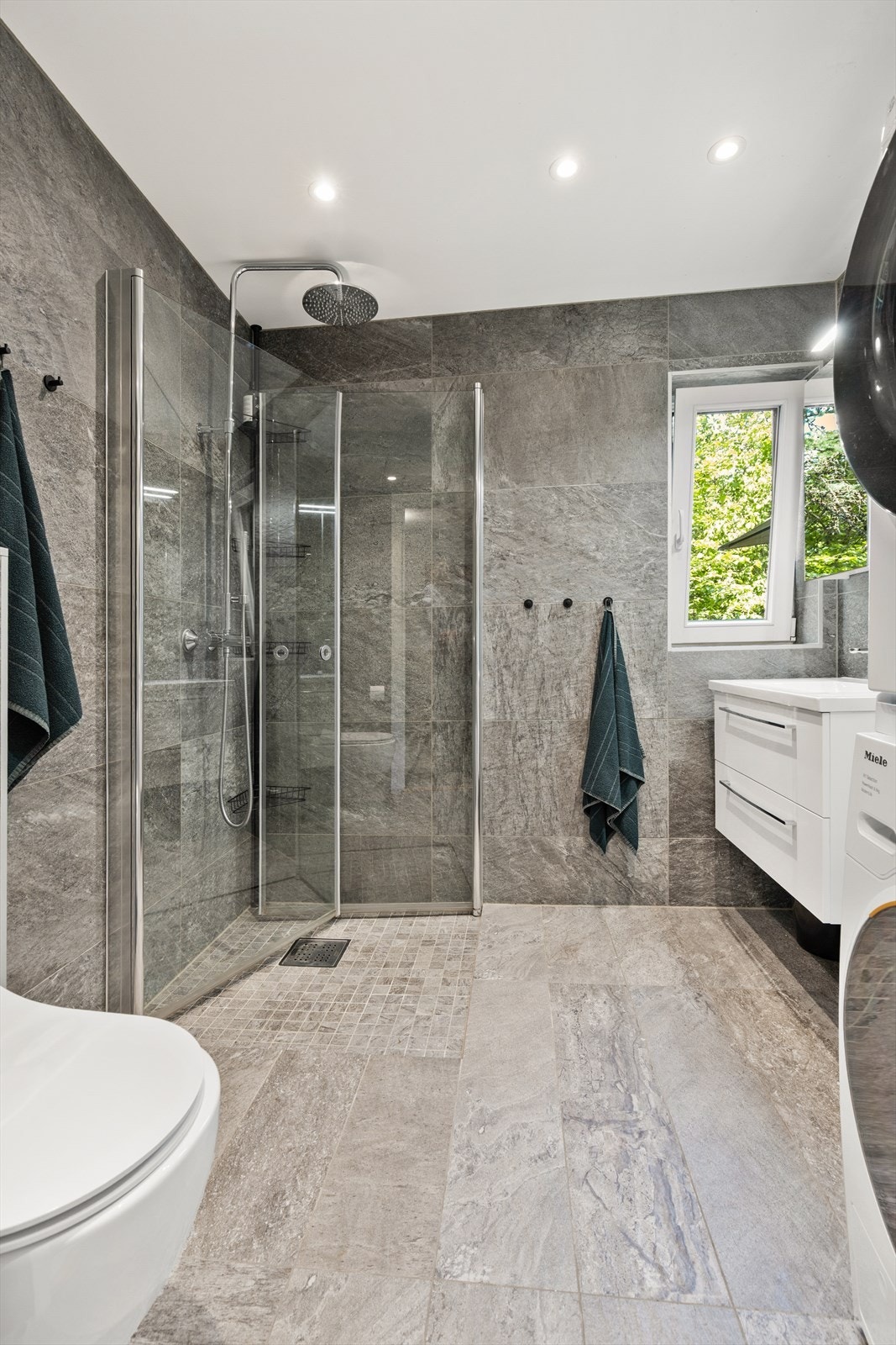 Badet er innredet med vegghengt klosett, servant nedfelt i innredning, speilskap m/lys og dusjhjørne med svingbare glassdører. Galleribilde