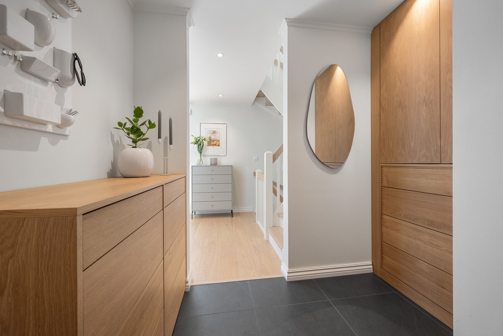 Innbydende hall med store fliser på gulvet og lekker plassbygget innredning i eik fra Tree Stories fra 2022. Galleribilde