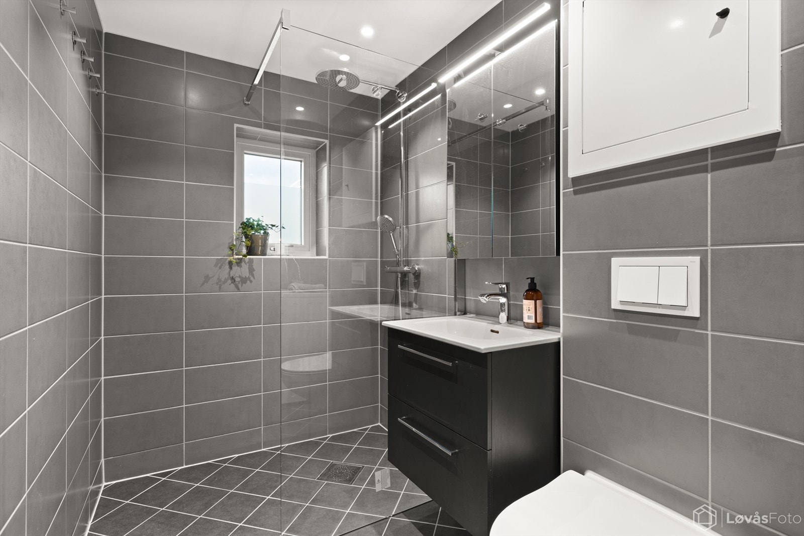 Badet har en romslig dusjsone, servant med innredning og varmekabler i gulv. Galleribilde