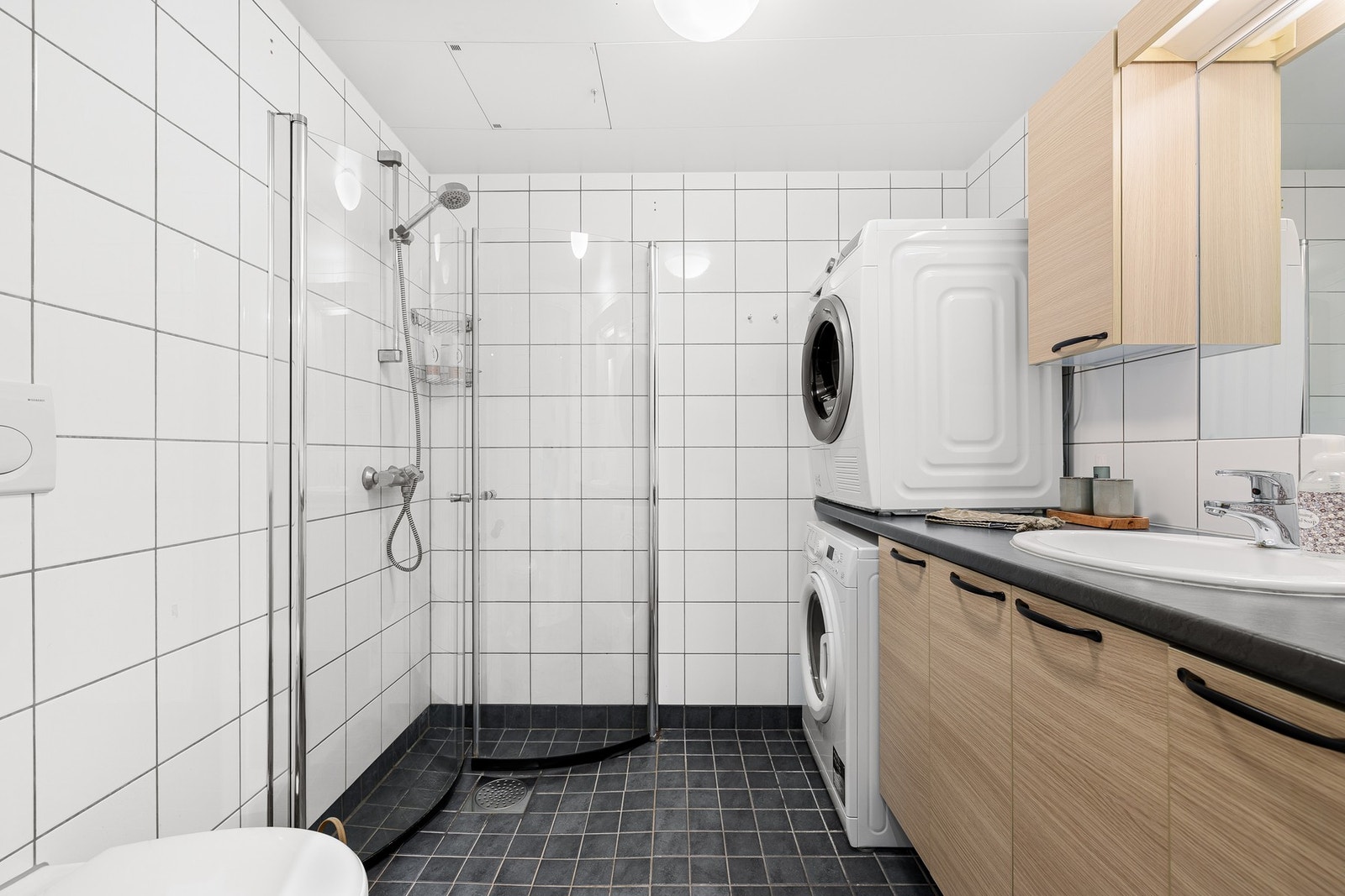 Plassbesparende og innfellbare dusjdører i glass, opplegg for vaskemaskin og tørketrommel, veggmontert wc, servant på underskap, overskap og speil. Galleribilde