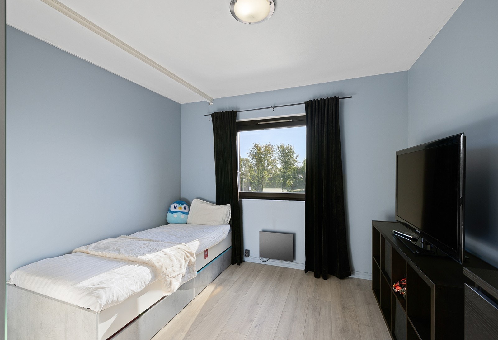 Soverom 3 - Et lyst og trivelig soverom som er malt i en behagelig blå tone som skaper en rolig atmosfære, og det store vinduet slipper inn rikelig med naturlig lys. Galleribilde