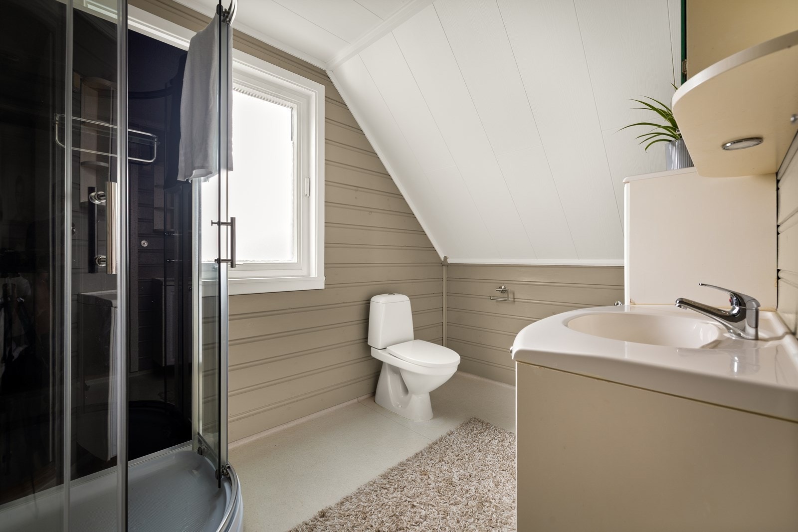 Servantinnredning og wc er plassert mot skråtaket, med panel på vegger og belegg på gulv. Galleribilde