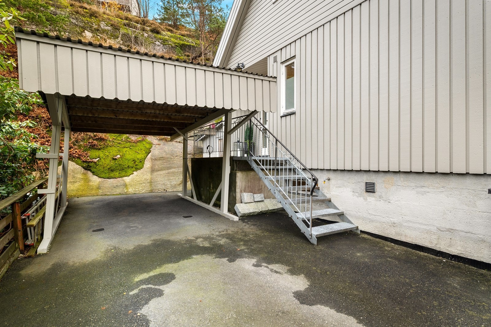 Carport med asfaltert dekke gir praktisk parkeringsmulighet, og trapp opp til inngangspartiet. Galleribilde