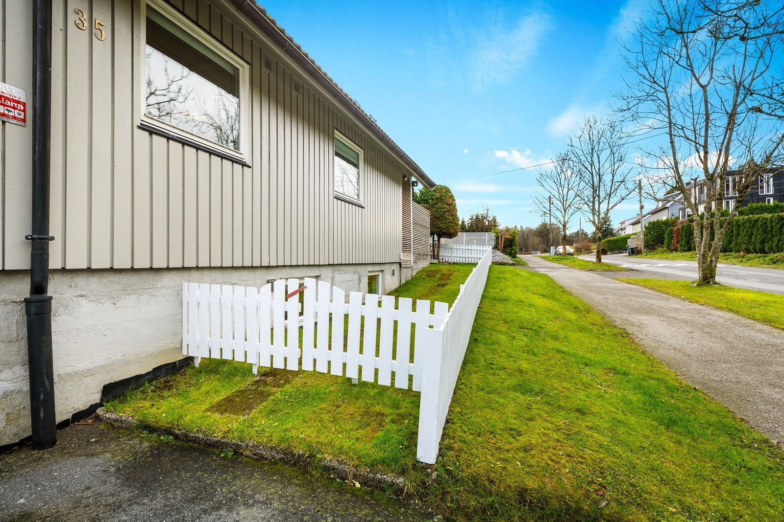 Det er en asfaltert gårdsplass med lett skrående tomt opparbeidet med hage og beplantning. Galleribilde