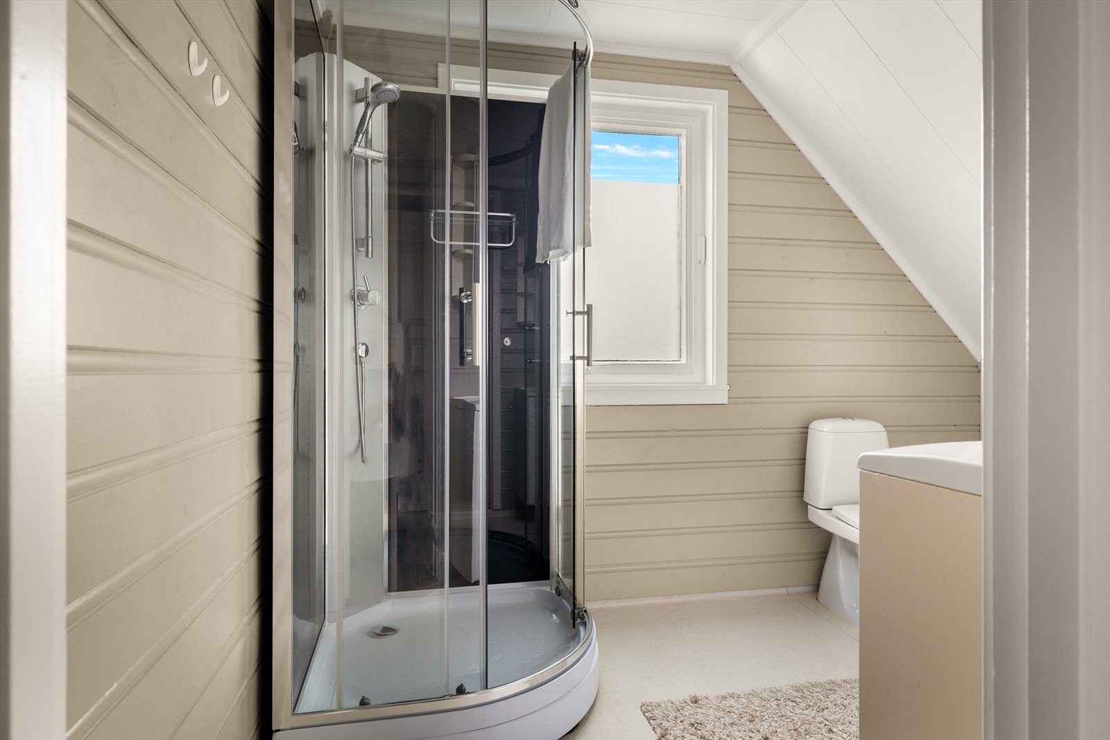 Dusjkabinett og wc er plassert ved vinduet, med panel på vegger og belegg på gulv. Galleribilde