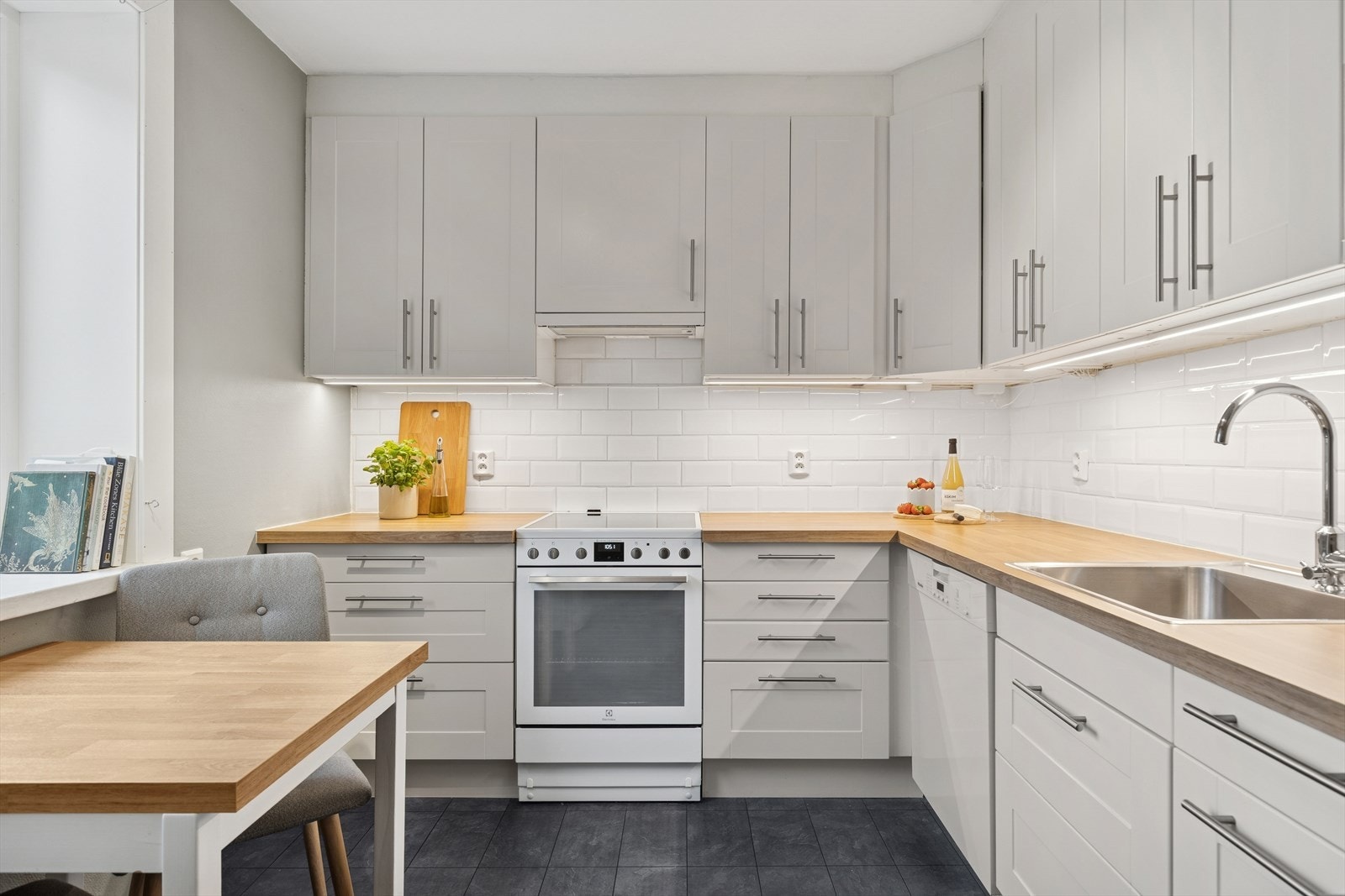 Kjøkkenet har belysning under overskap, flis på vegg, opplegg for oppvaskmaskin og laminat benkeplate (2022) med nedfelt kum i rustfritt stål. Galleribilde