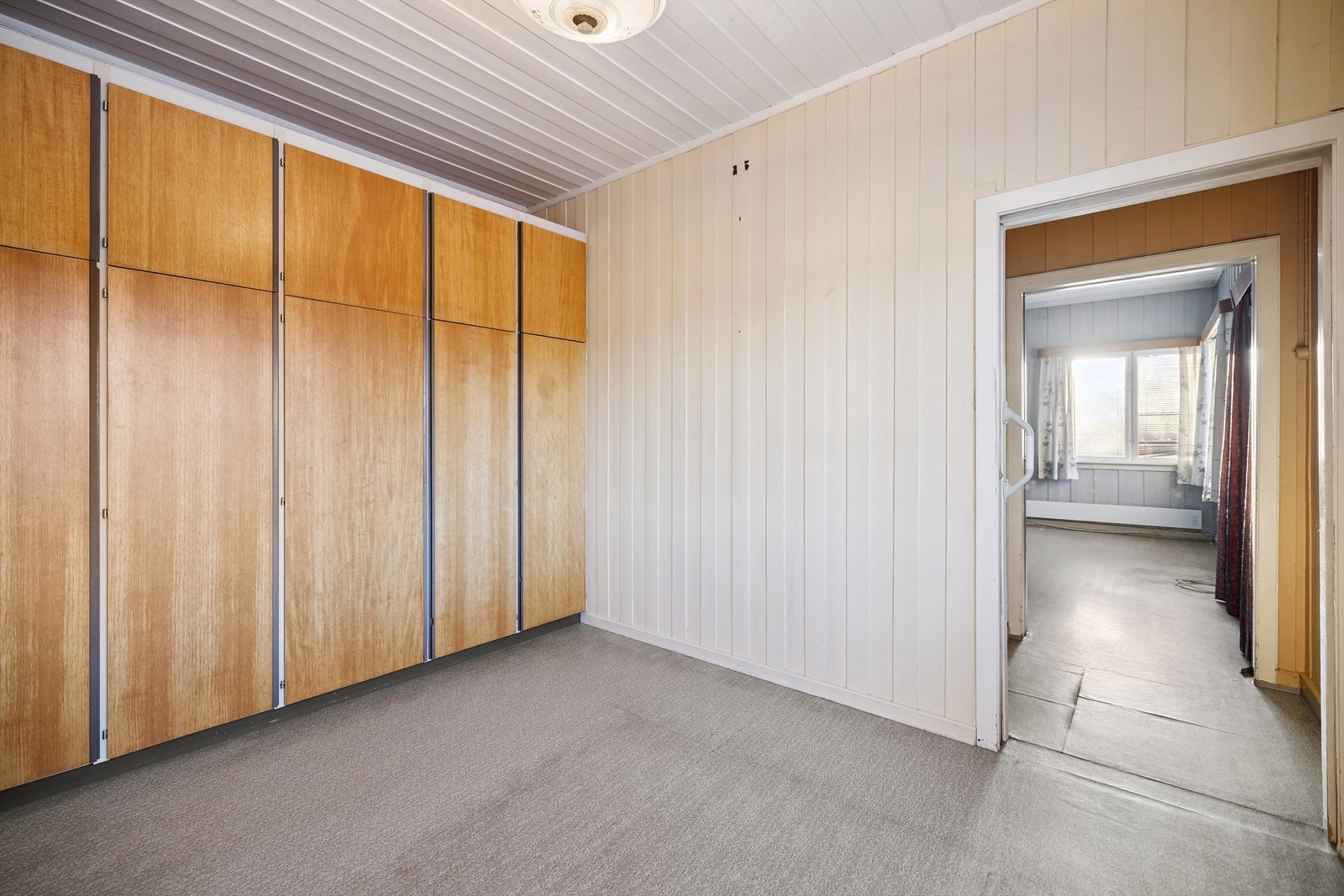 Soverom i første etasje med plassbygde garderobeskap og malt trepanel. Galleribilde